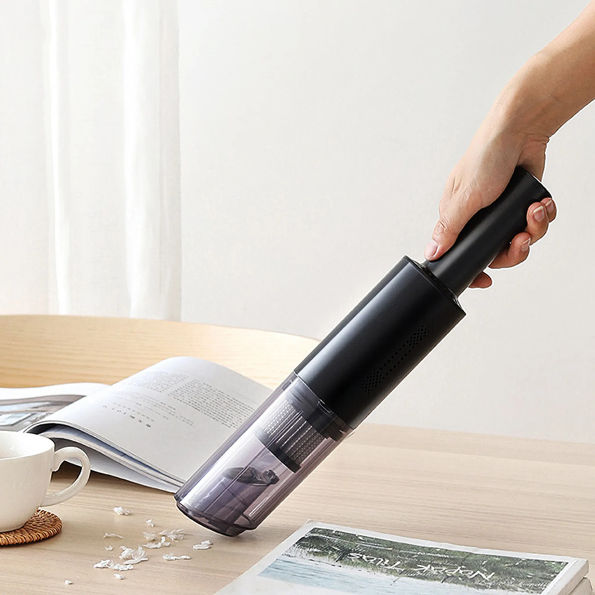 Eine Hand hält einen schwarzen und transparenten Handstaubsauger über einem Holztisch.