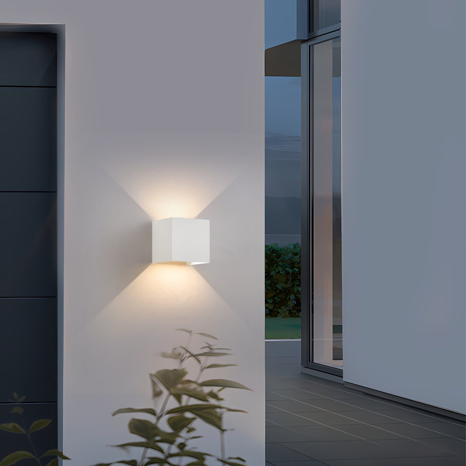 Un'applique da esterno bianca a forma di cubo su un muro, con una pianta di lato e una porta visibile.