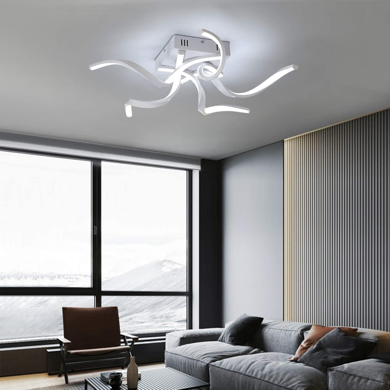 Ein modernes Wohnzimmer mit weißer Deckenleuchte mit geschwungenen Armen, grauem Sofa und großem Fenster.