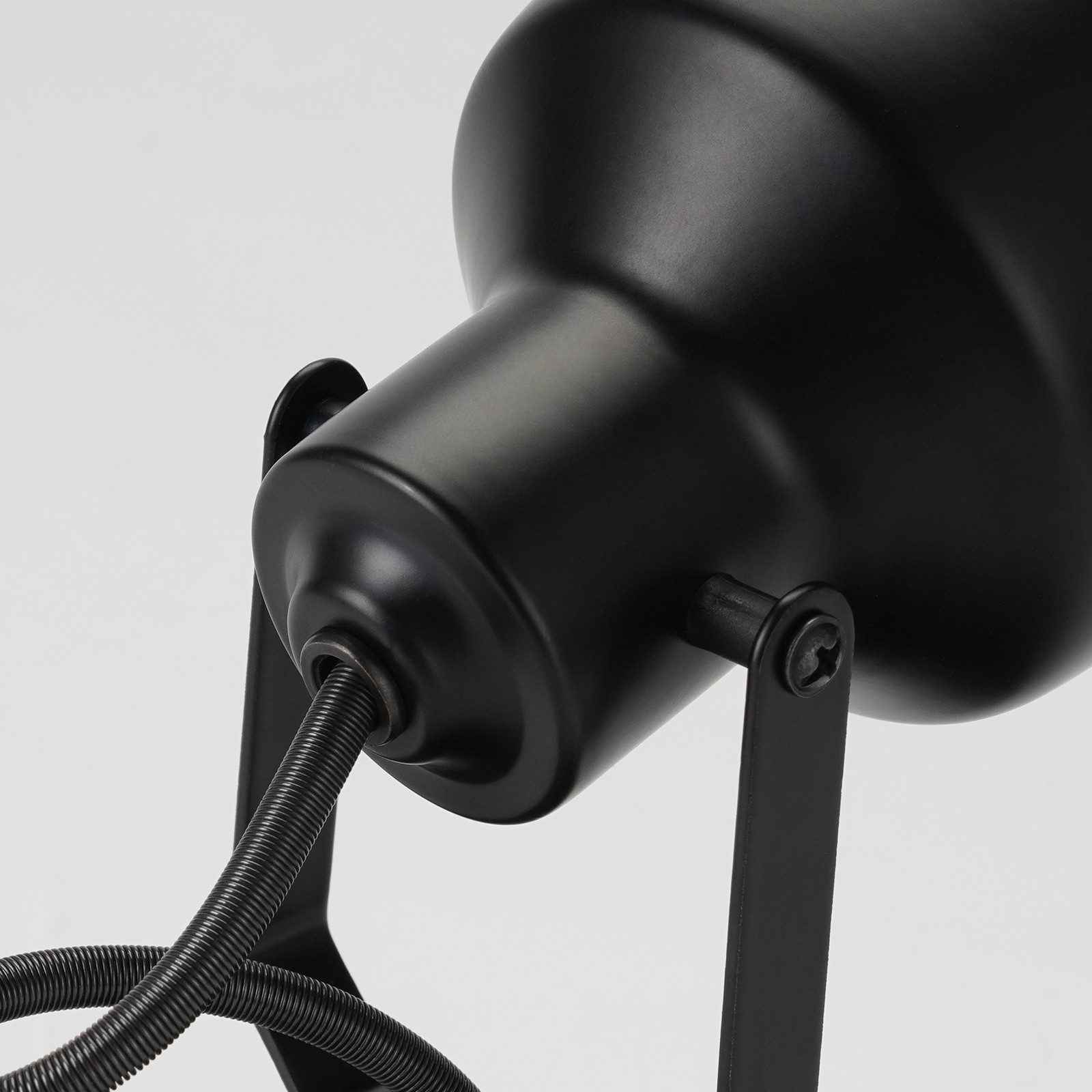 Szczegół czarnej lampy, pokazujący podstawę, przewód i samą lampę.