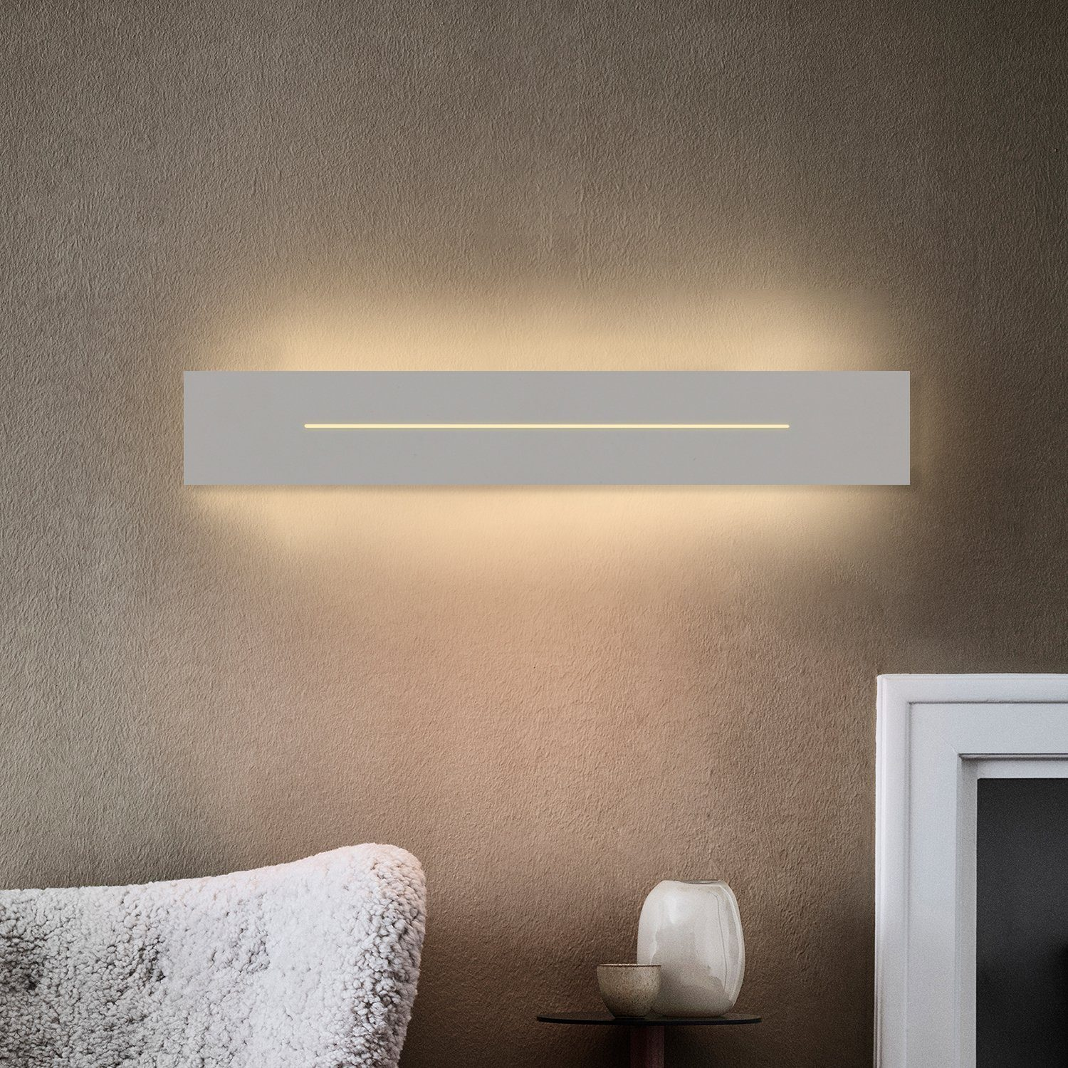 Una lampada da parete rettangolare bianca con linea di luce su un muro marrone, con tavolino e vaso.