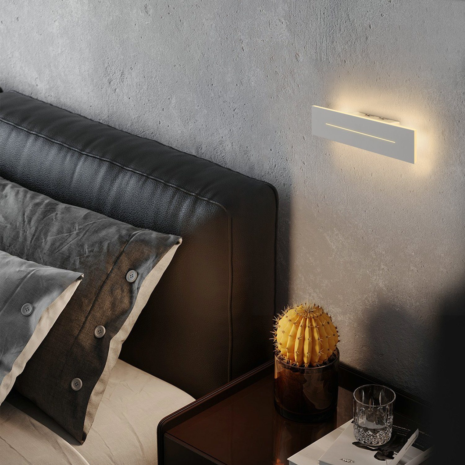 Una camera da letto con lampada a parete, letto, cuscini e un cactus.