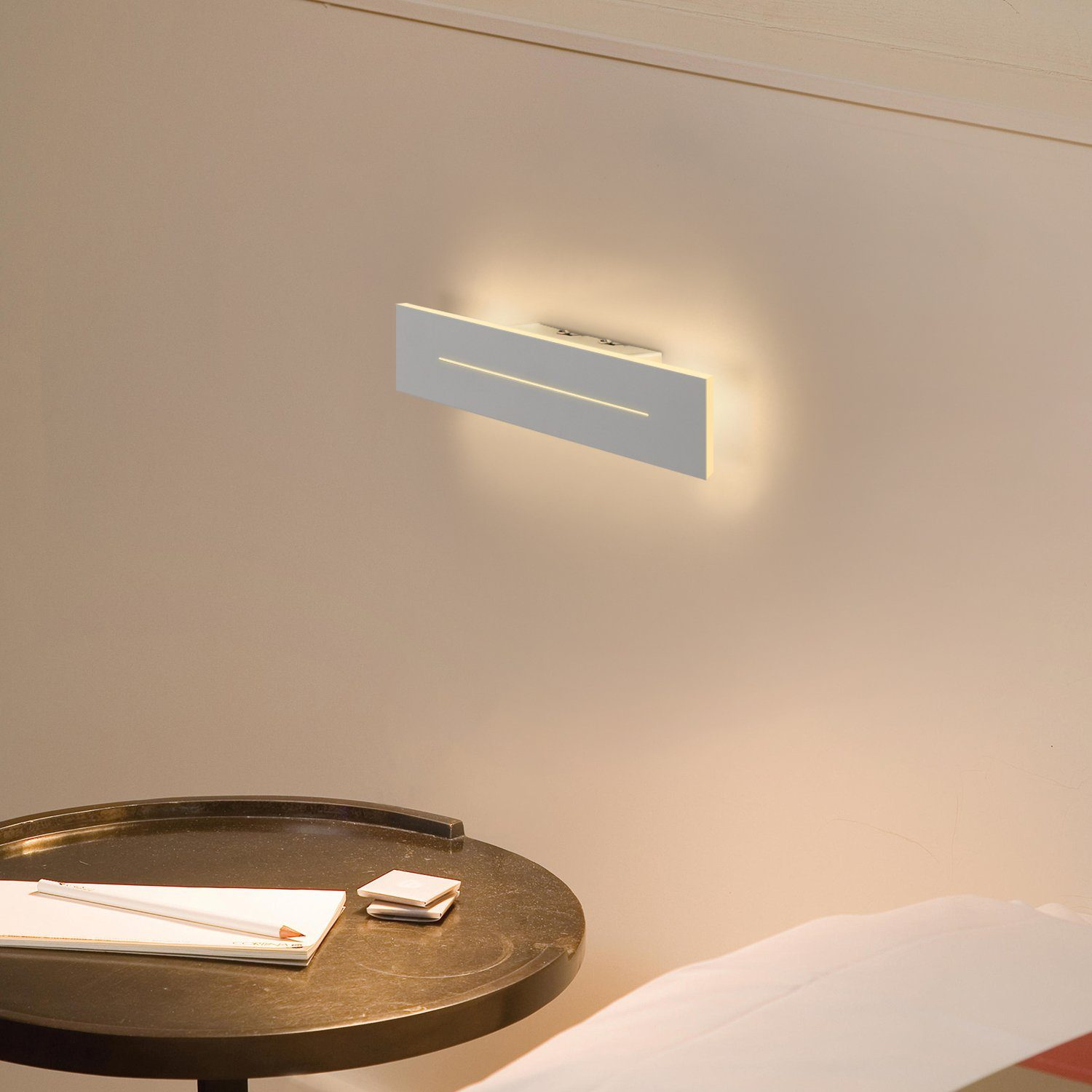 Un muro con un apparecchio di illuminazione rettangolare bianco. Un tavolino con oggetti davanti al muro.