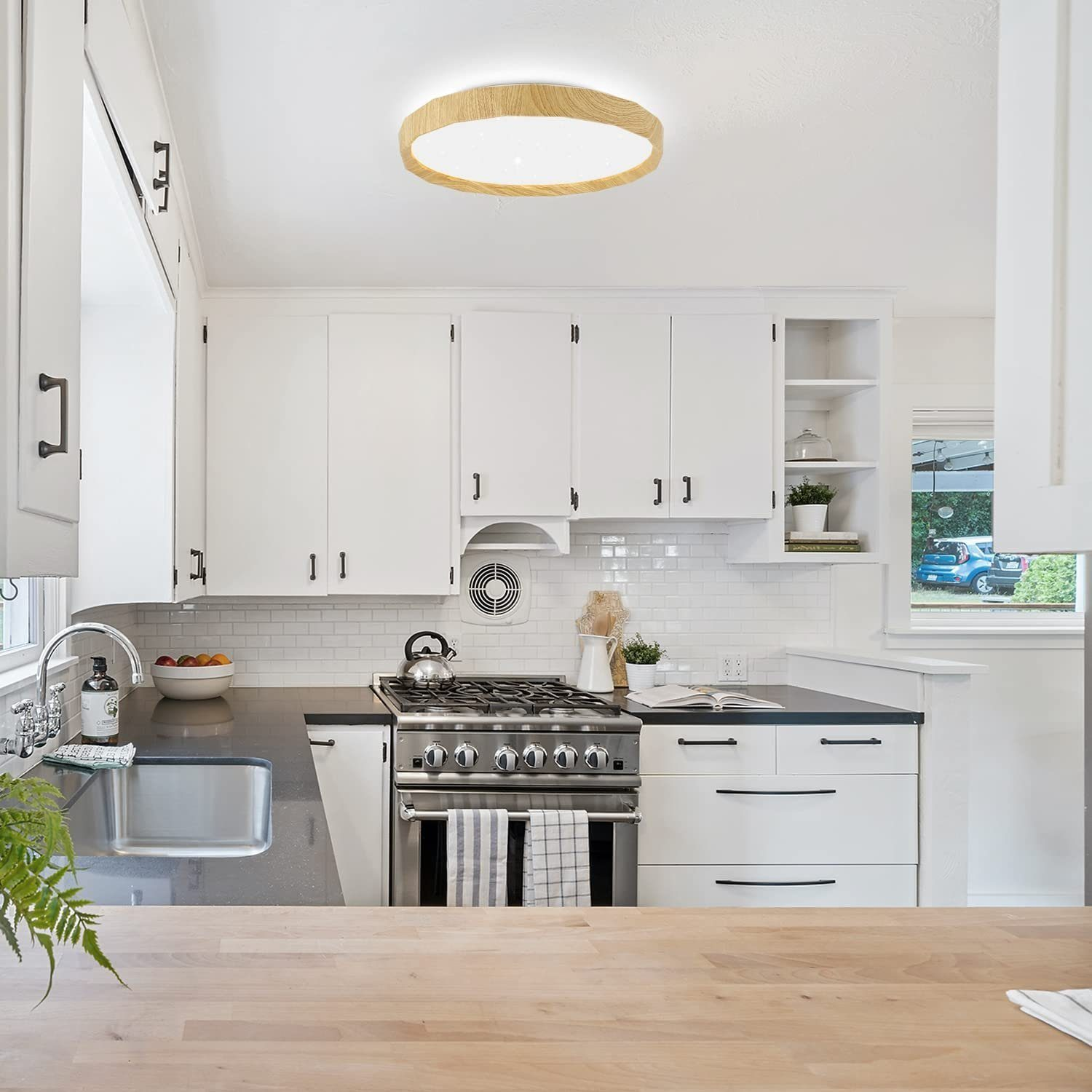 Cocina luminosa con gabinetes blancos, encimera de madera y luz de techo redonda.