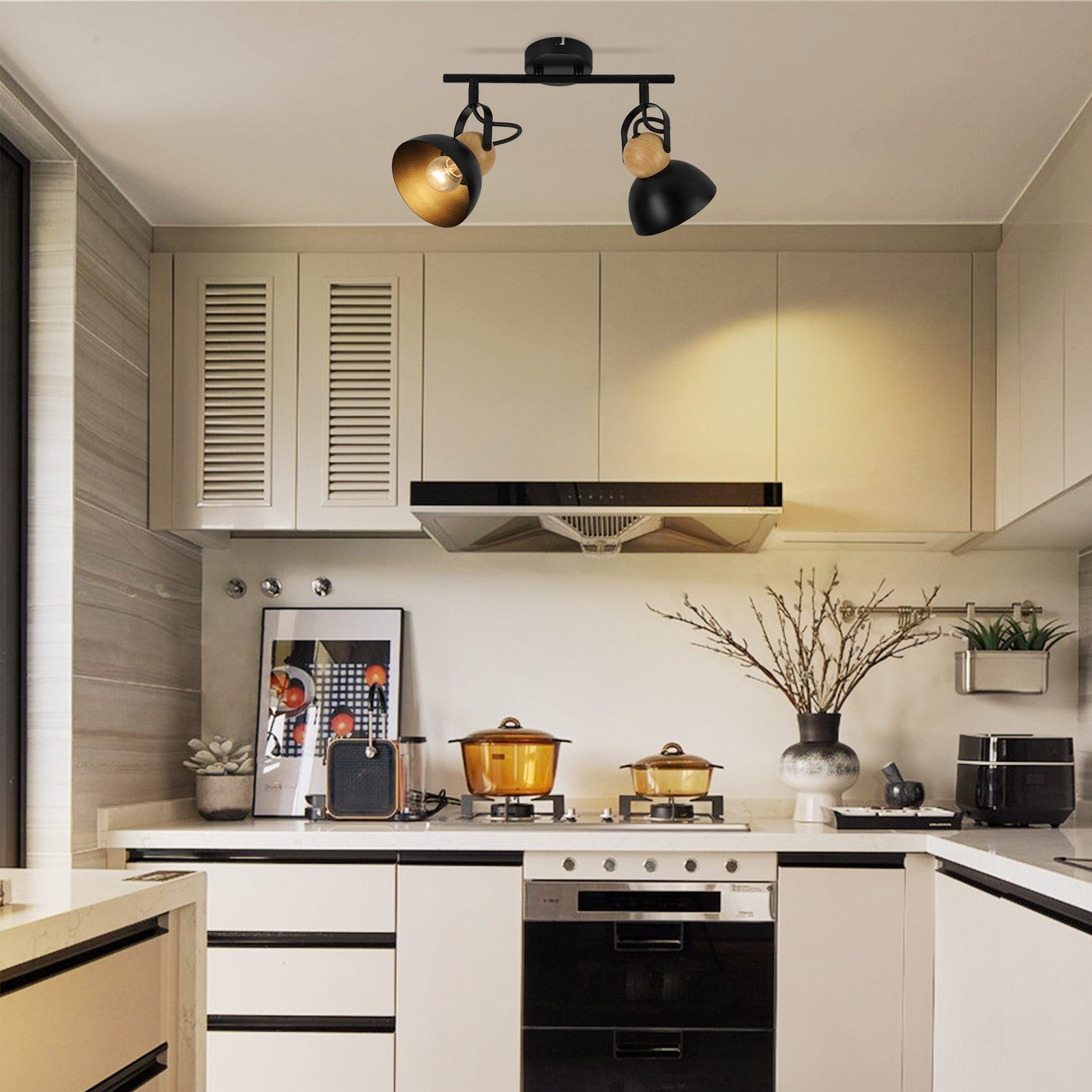 Kuchnia z białymi szafkami, kuchenką i oświetleniem górnym. Garnki na kuchence, grafika na ścianie i okap.