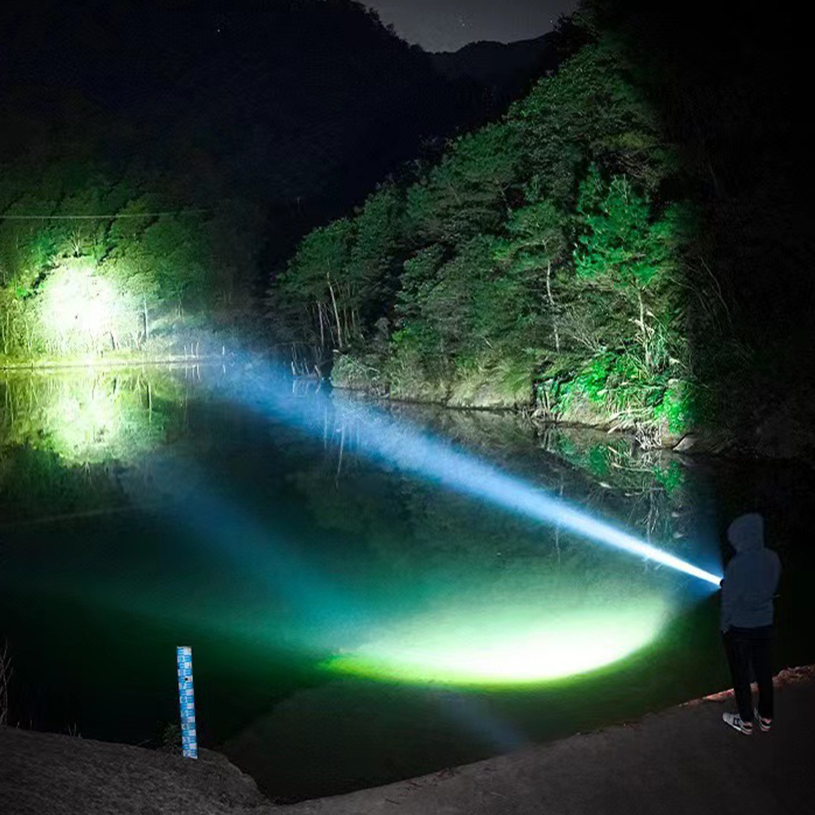 Person leuchtet nachts mit Taschenlampe auf Wasser. Grünes Leuchten.