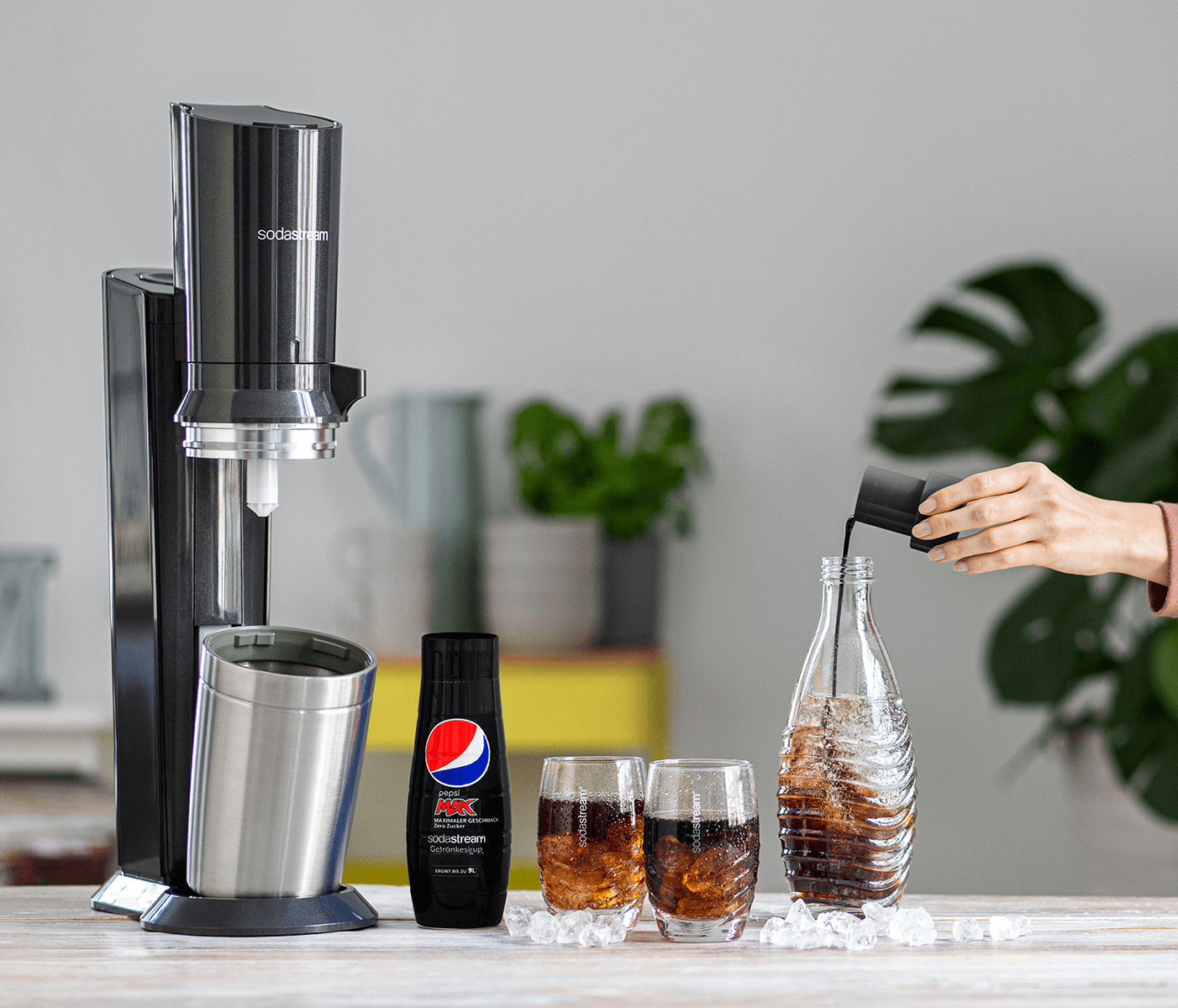 Ein Sodabereiter mit einer befüllten Flasche, zwei Gläsern mit Soda und einer Pepsi Max Flasche.