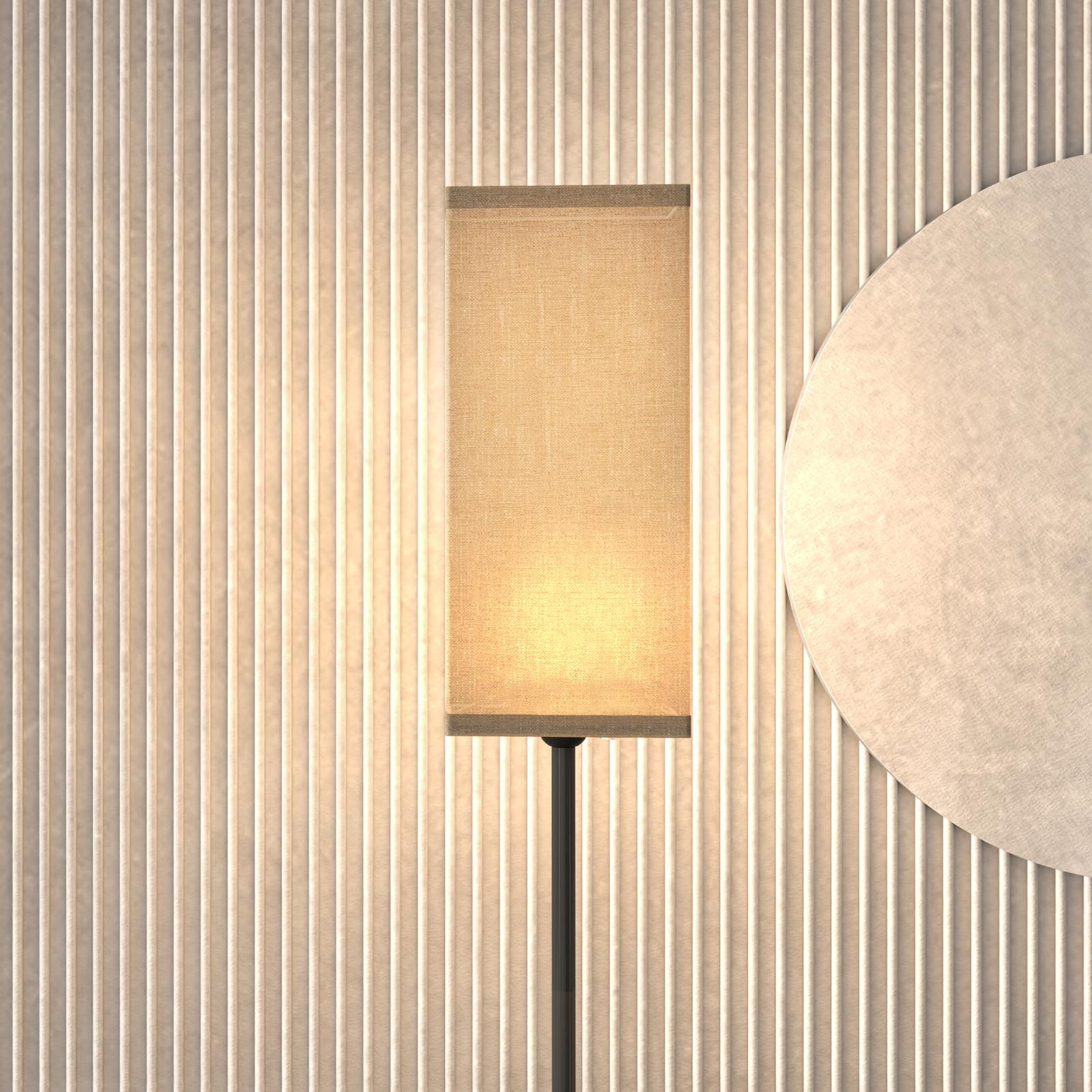 Eine Stehlampe mit beigem rechteckigem Schirm. Licht scheint von der Lampe zur Wand.