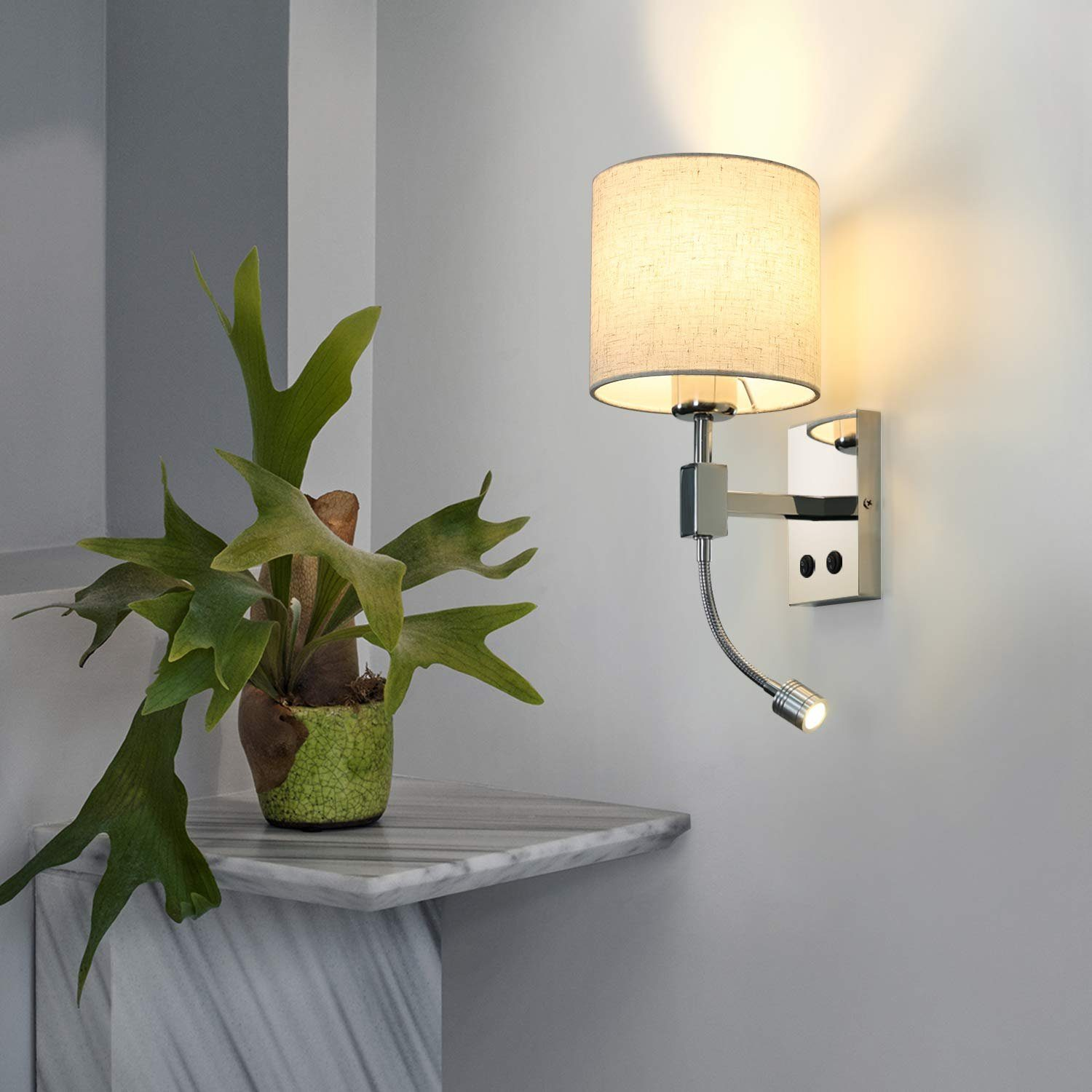 Eine Lampe an einer Wand, neben einer Pflanze auf einem Marmorregal. Die Lampe hat einen flexiblen Arm.