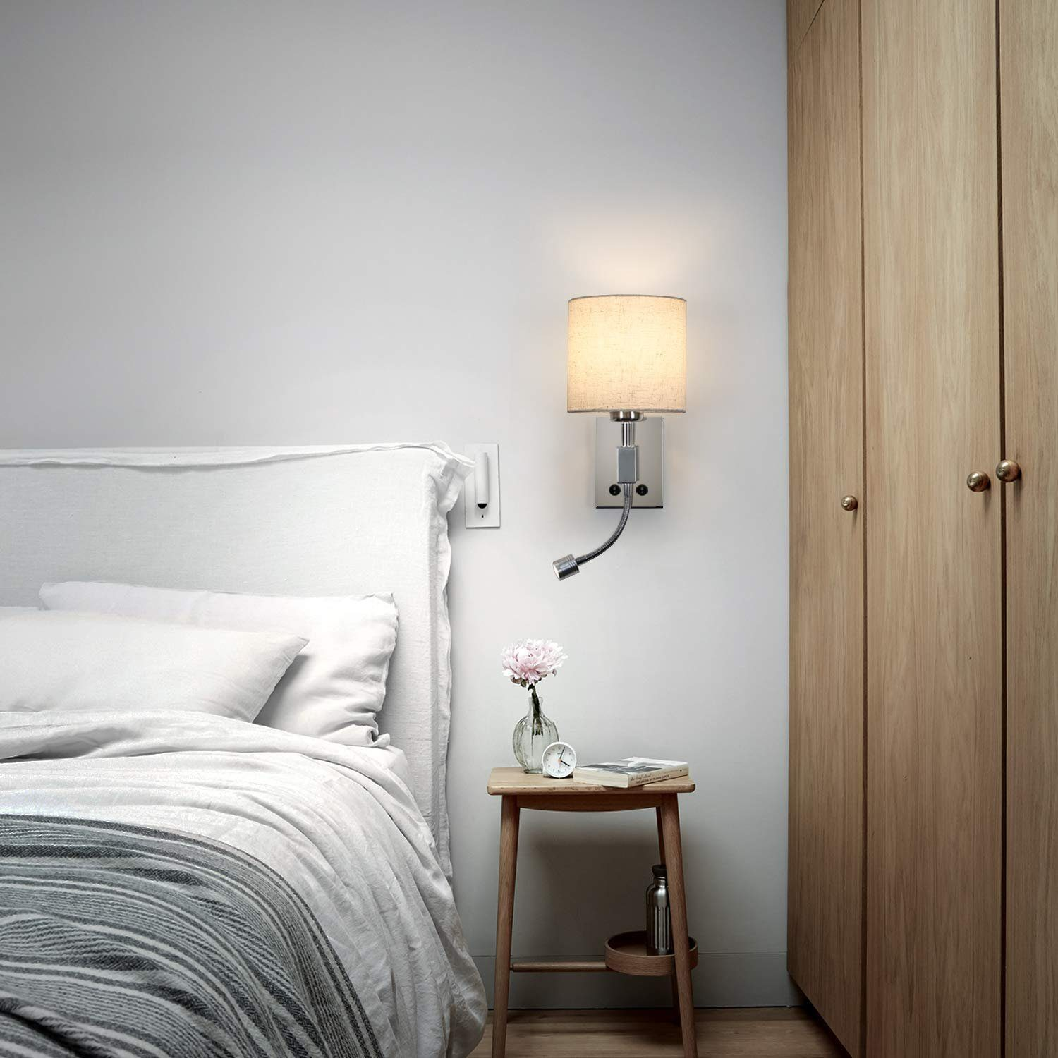 Ein Schlafzimmer mit Bett, Nachttisch und Wandlampe. Ein kleiner Tisch mit Vase.