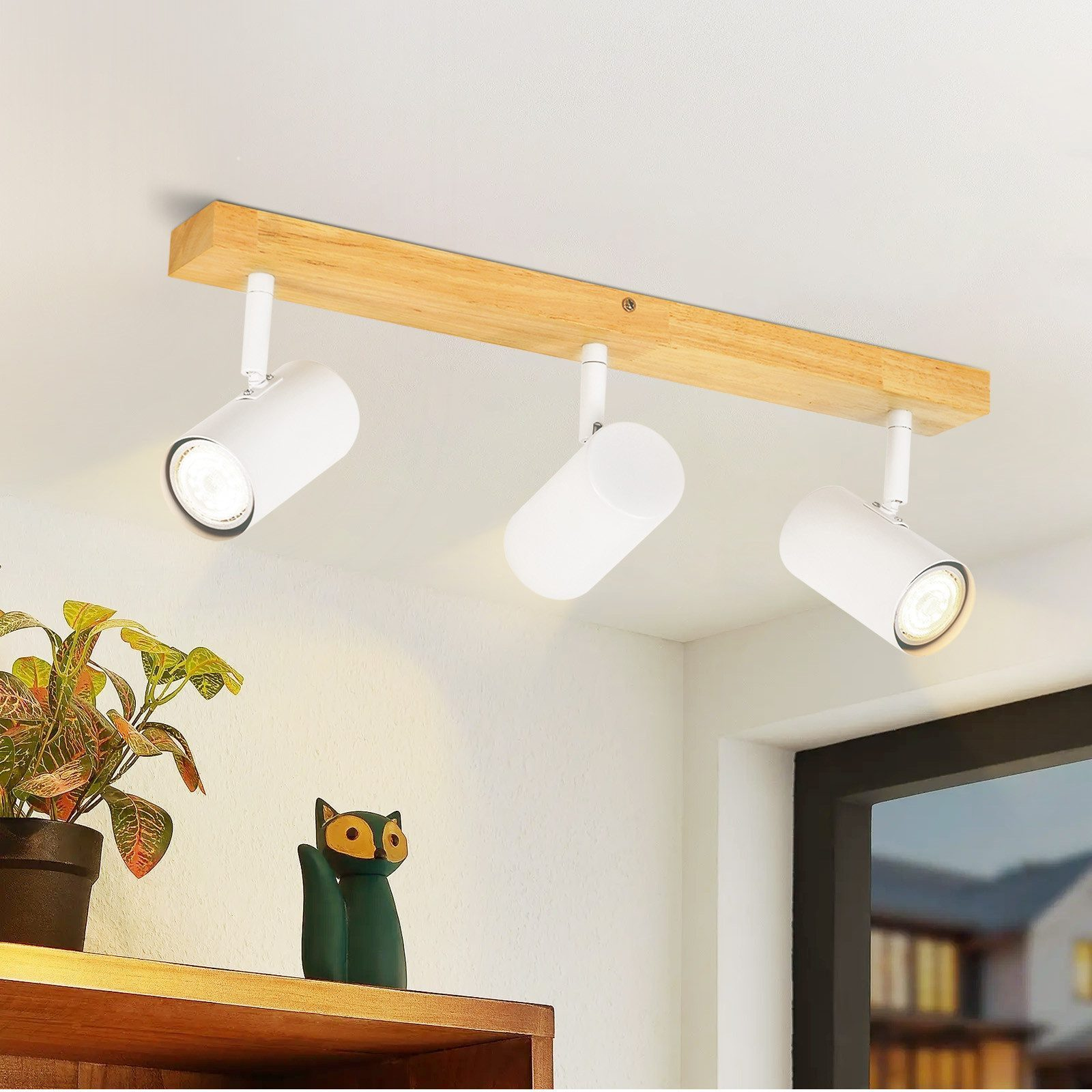 Un lampadario con tre faretti bianchi su una trave di legno, con una statua di gatto e piante.