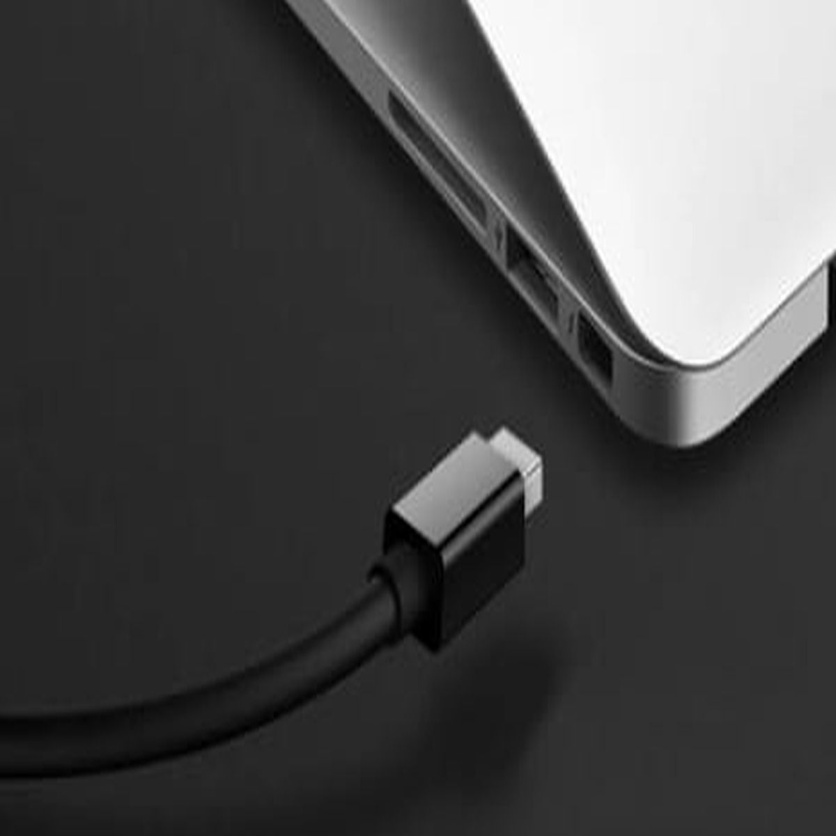 Czarny kabel USB-C podłączony do laptopa na ciemnej powierzchni.
