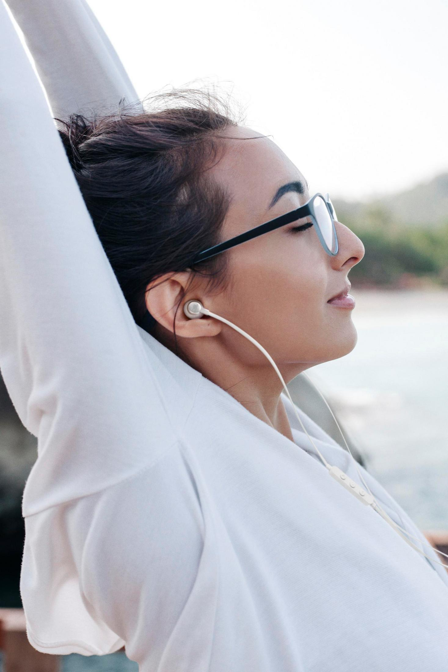 Kobieta w okularach i białej bluzie z kapturem ma na sobie białą słuchawkę i rozciąga się.