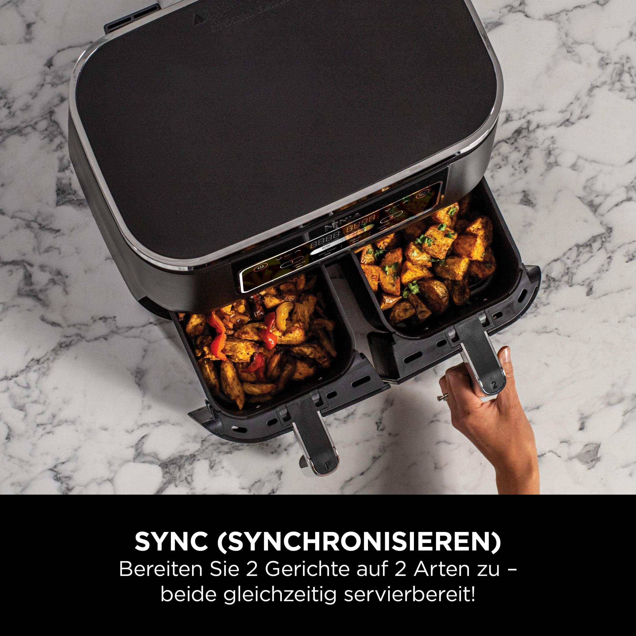 Czarna frytkownica powietrzna z dwoma przegródkami, z jedzeniem w środku. Ręka wyciąga tacę.