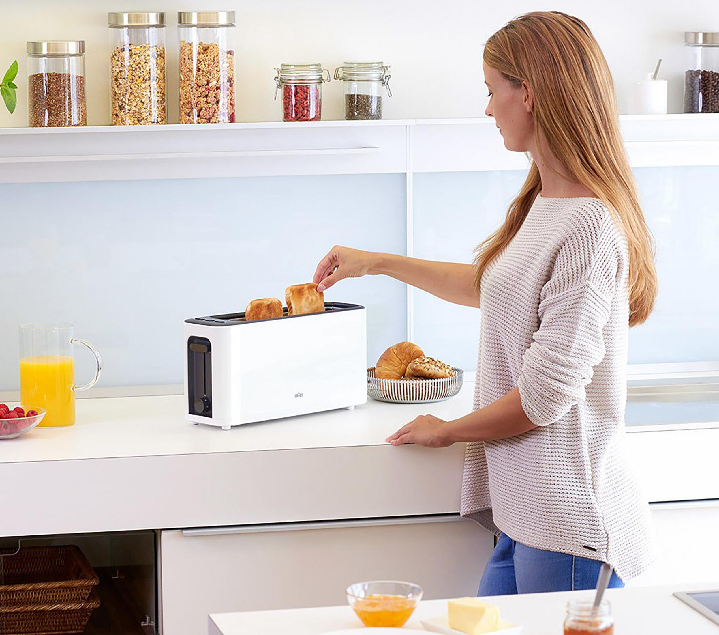 Kobieta wkłada tosty do białego tostera na blacie. Widoczne inne produkty spożywcze.