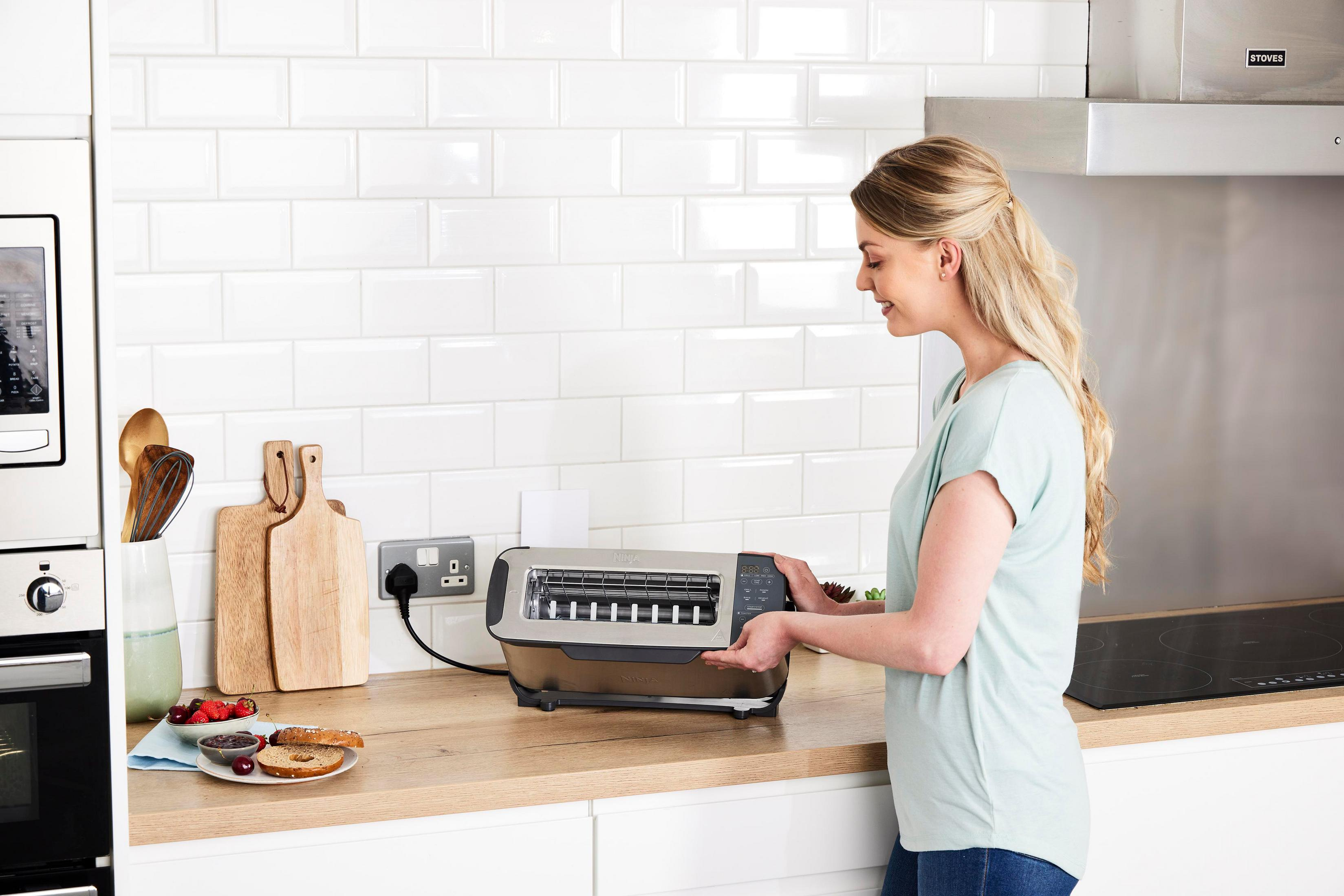 Kobieta używa tostera w kuchni. Kromki chleba i dżem na blacie.