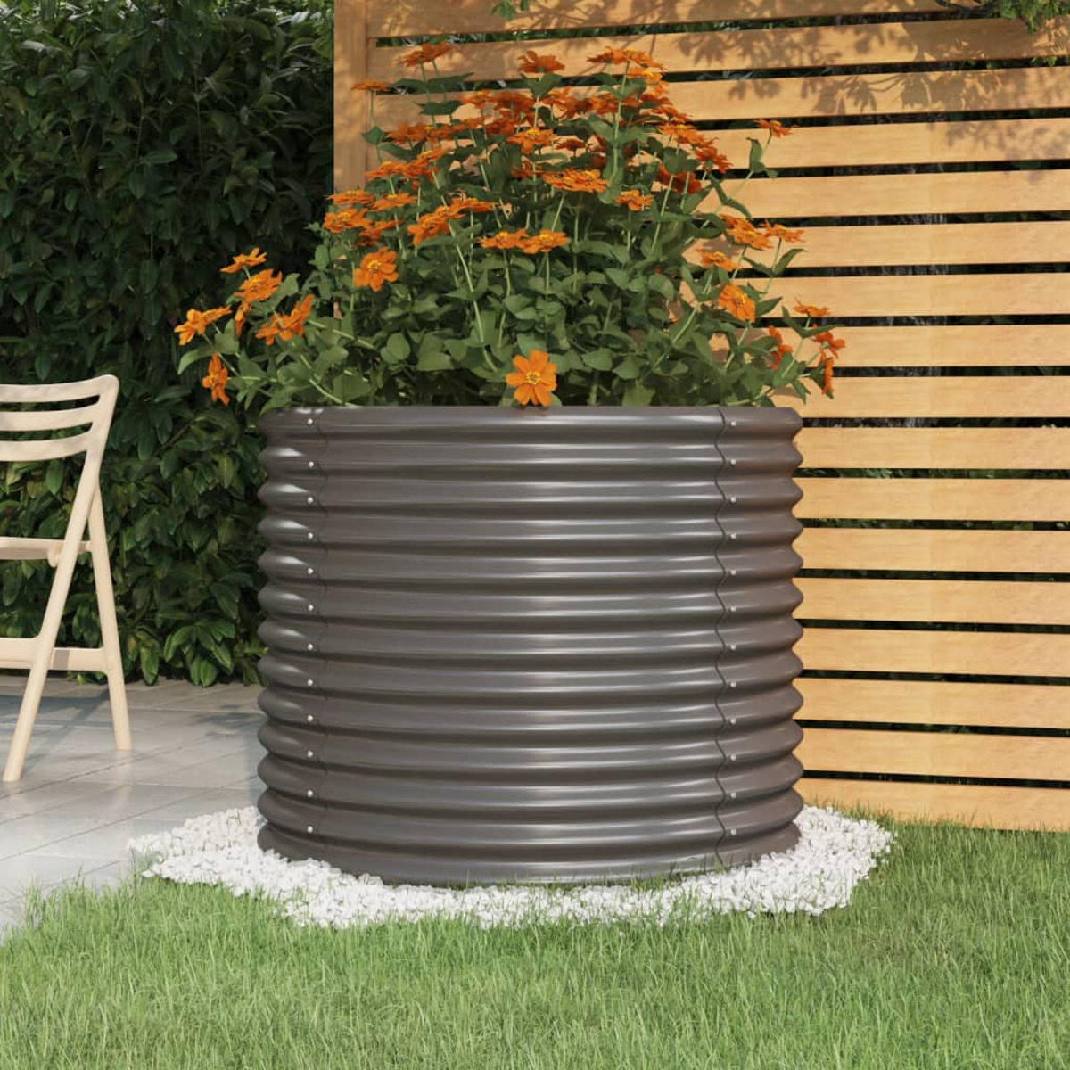 Ein Metall-Gartenpflanzer mit orangefarbenen Blumen. Der Pflanzer ist dunkelgrau, umgeben von weißen Steinen.
