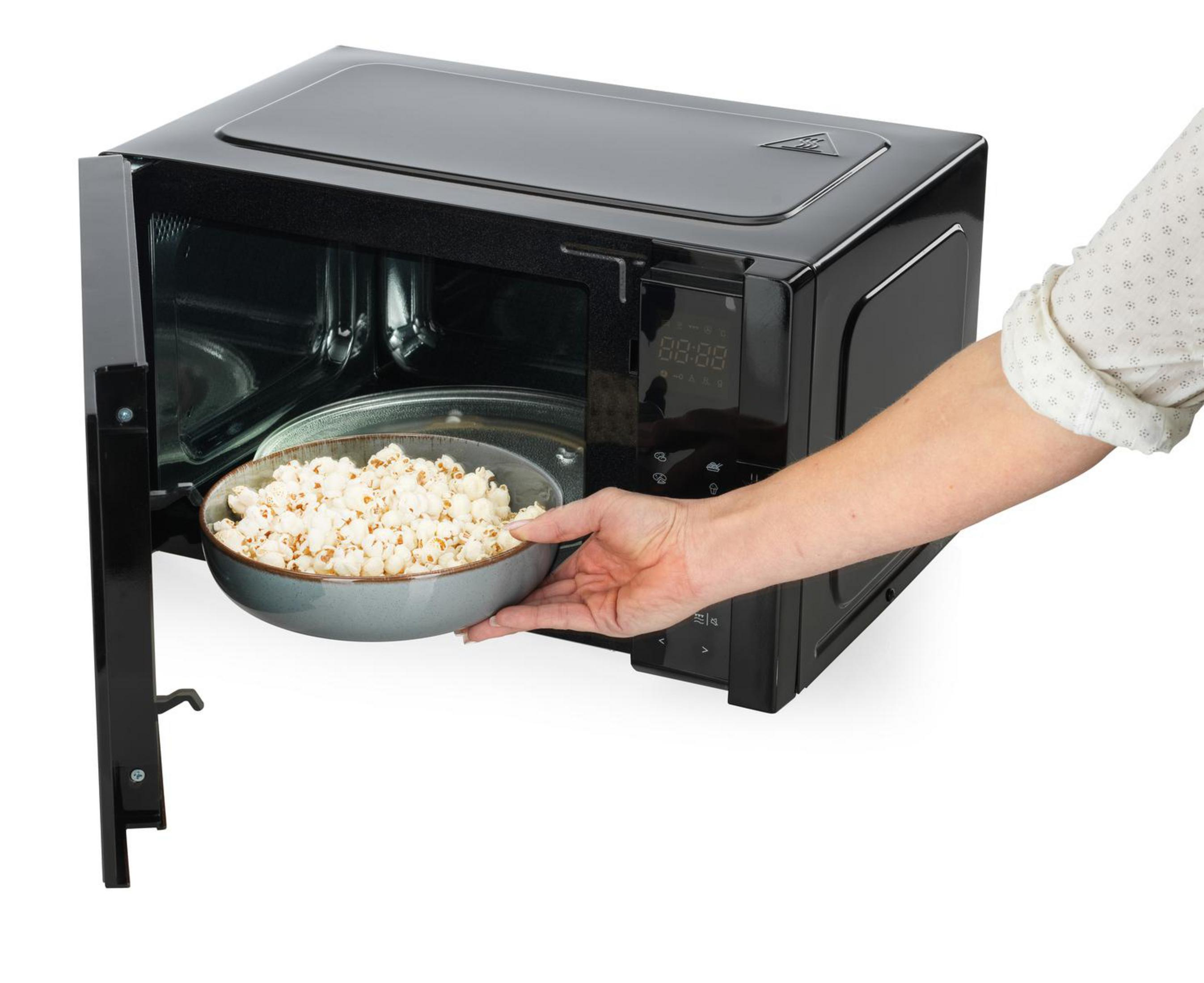 Ręka wyjmująca miskę popcornu z czarnej kuchenki mikrofalowej.