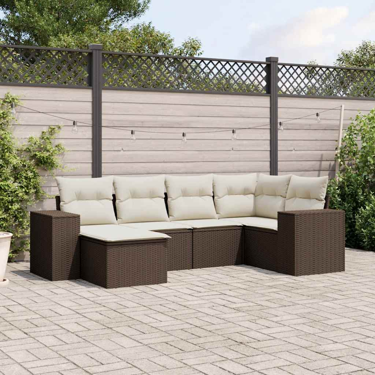 Divano angolare da esterno in rattan marrone con cuscini beige, su un patio pavimentato, con una recinzione sullo sfondo.