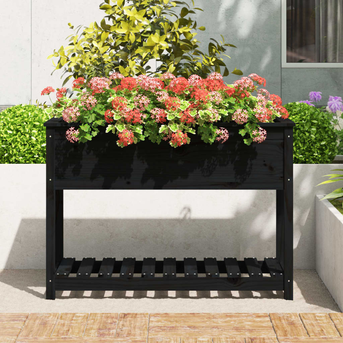 Schwarzer Holzpflanzkasten mit roten und rosa Blumen, vor einer weißen Wand, mit Grün im Hintergrund.