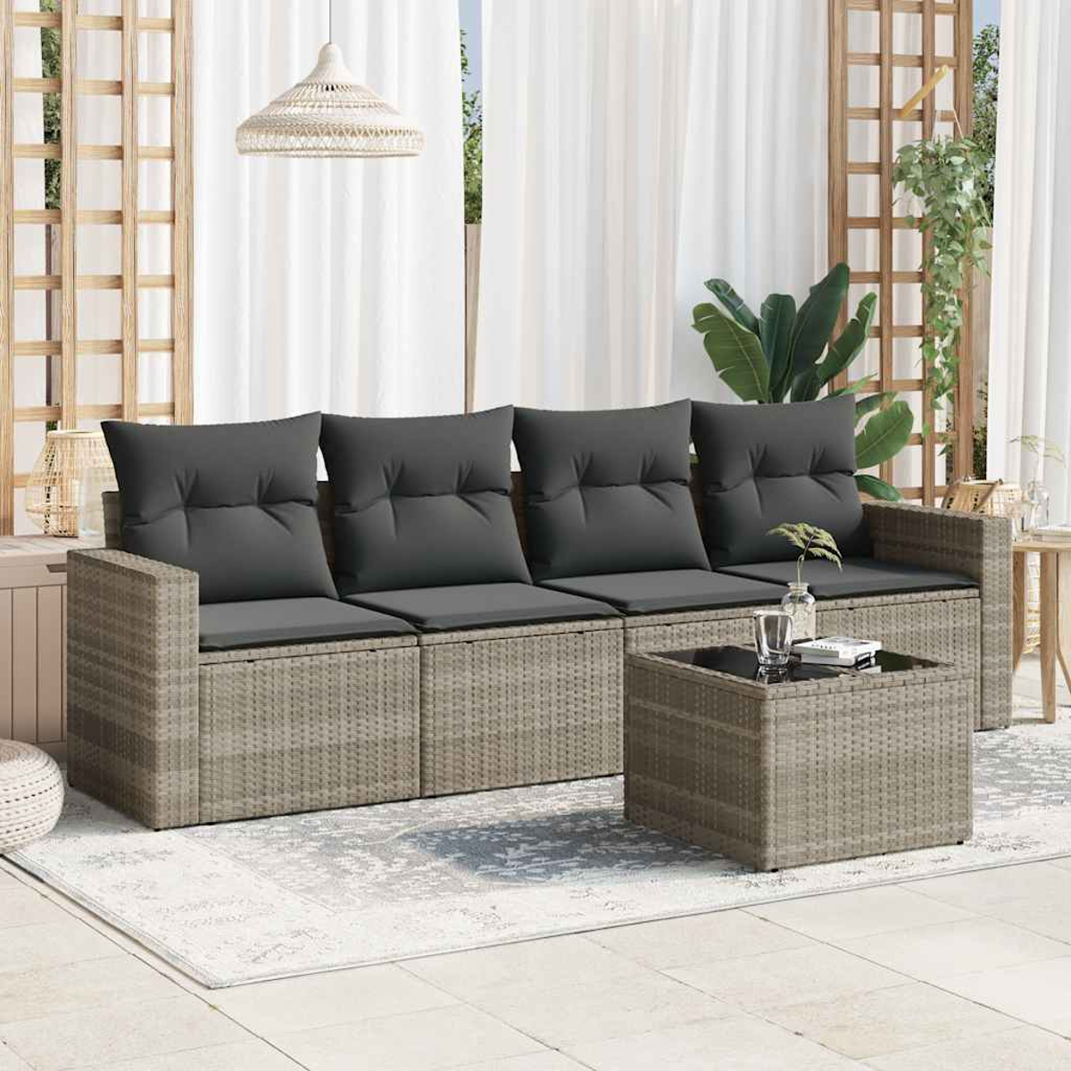 Set divano in rattan da esterno con cuscini grigi e tavolino. La scena è su un patio con tende bianche.
