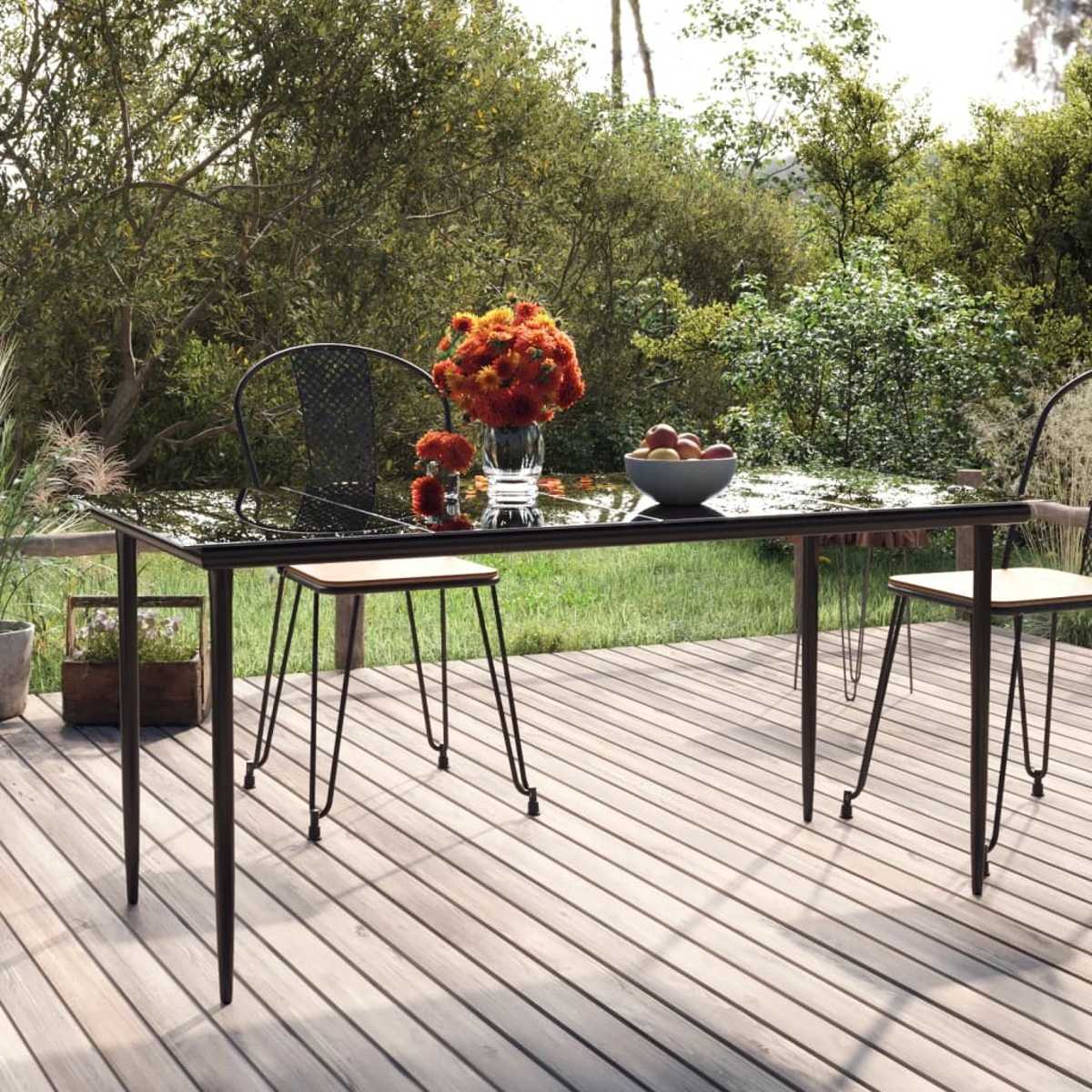 Esstisch im Freien mit Stühlen. Der Tisch ist aus Glas und hat Blumen und Obst. Holzterrasse.