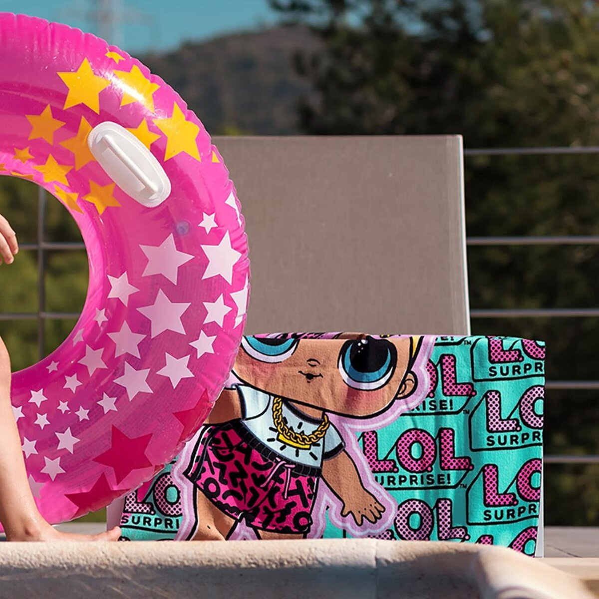 Un flotador rosa con estrellas y una toalla de muñeca LOL en una terraza de piscina.