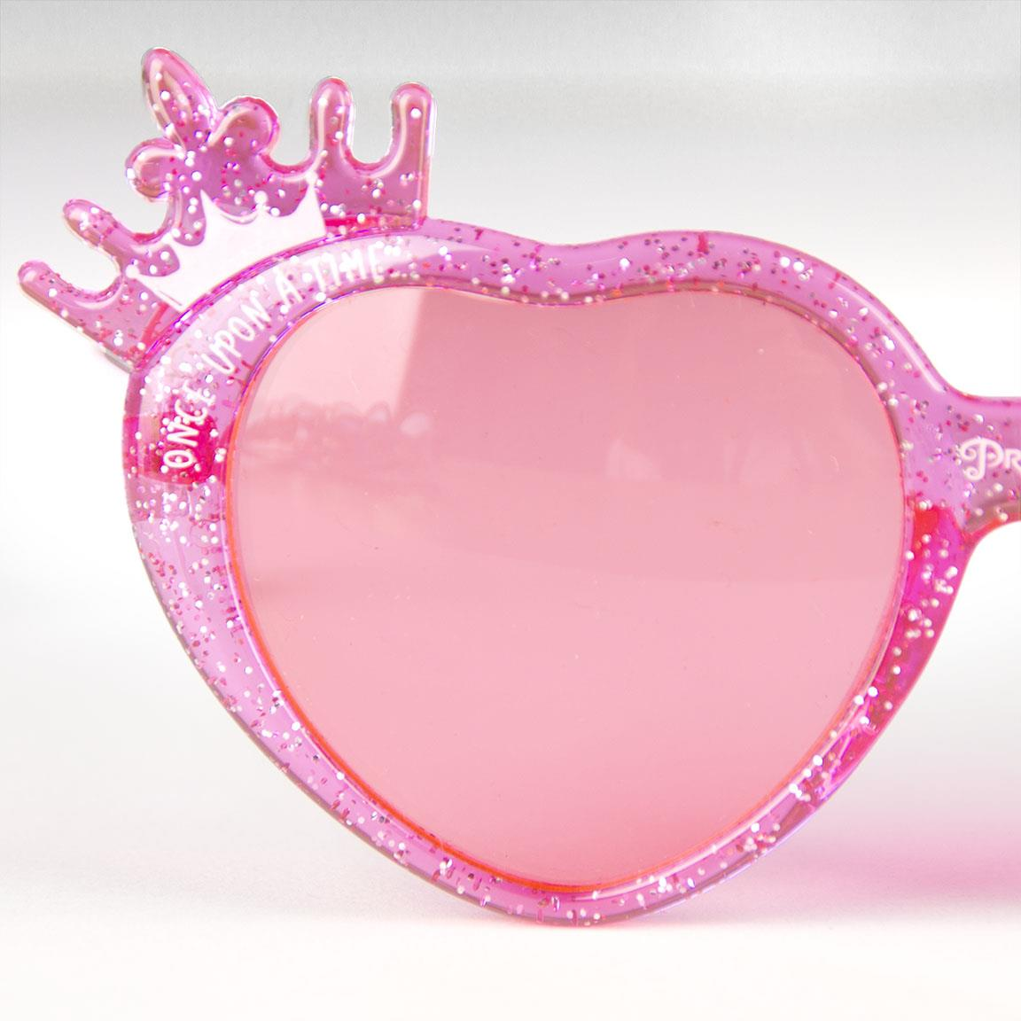 Primer plano de gafas de sol rosas en forma de corazón con detalle de corona, fondo blanco.