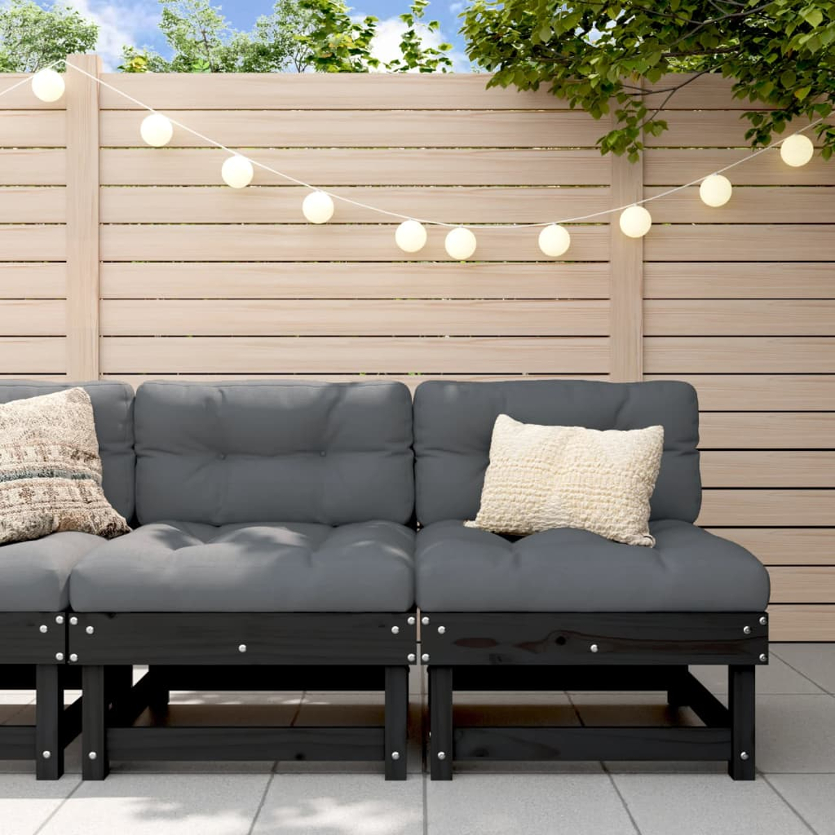 Ein Sofa mit dunkelgrauen Kissen und schwarzem Rahmen. Girlandenlichter hängen darüber.