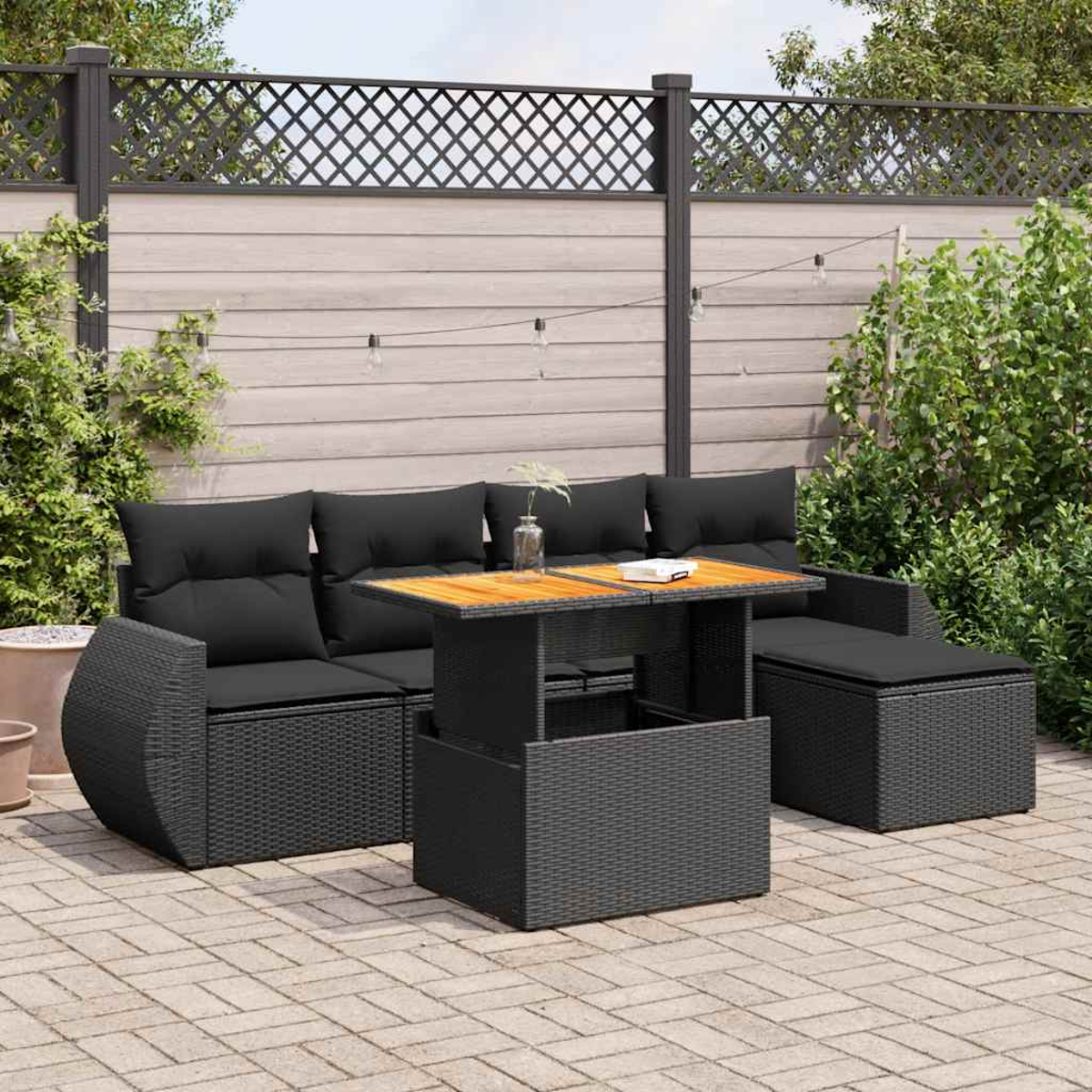 Mobili per patio esterno: un divano in vimini nero, due pouf e un tavolo su un patio pavimentato.