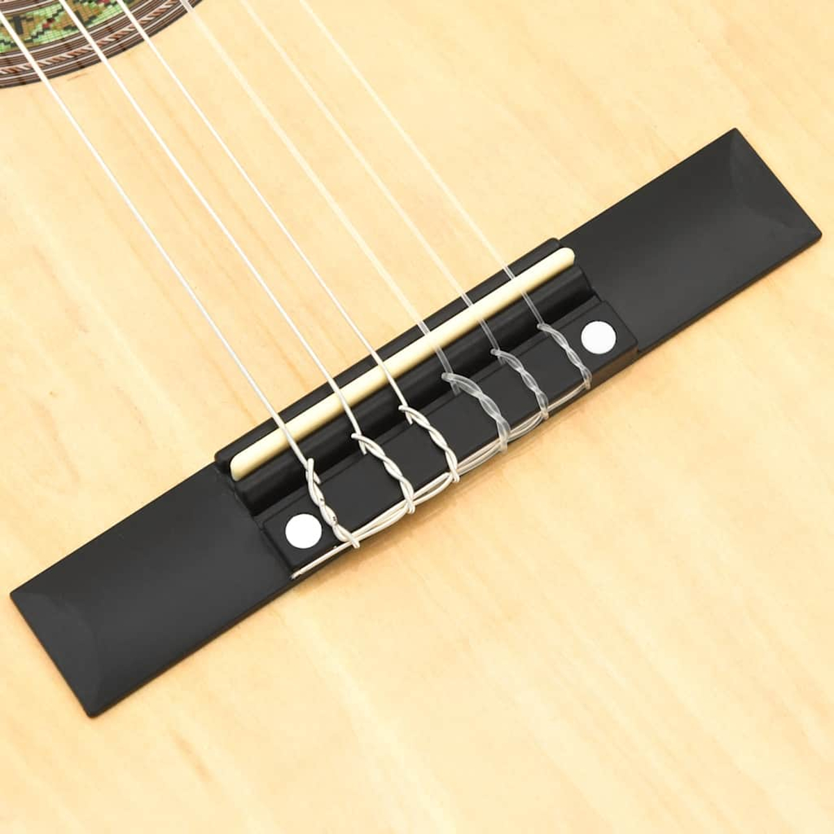 Nahaufnahme von Gitarrensteg und Saiten. Schwarzer Steg, sechs Saiten. Heller Holzuntergrund.