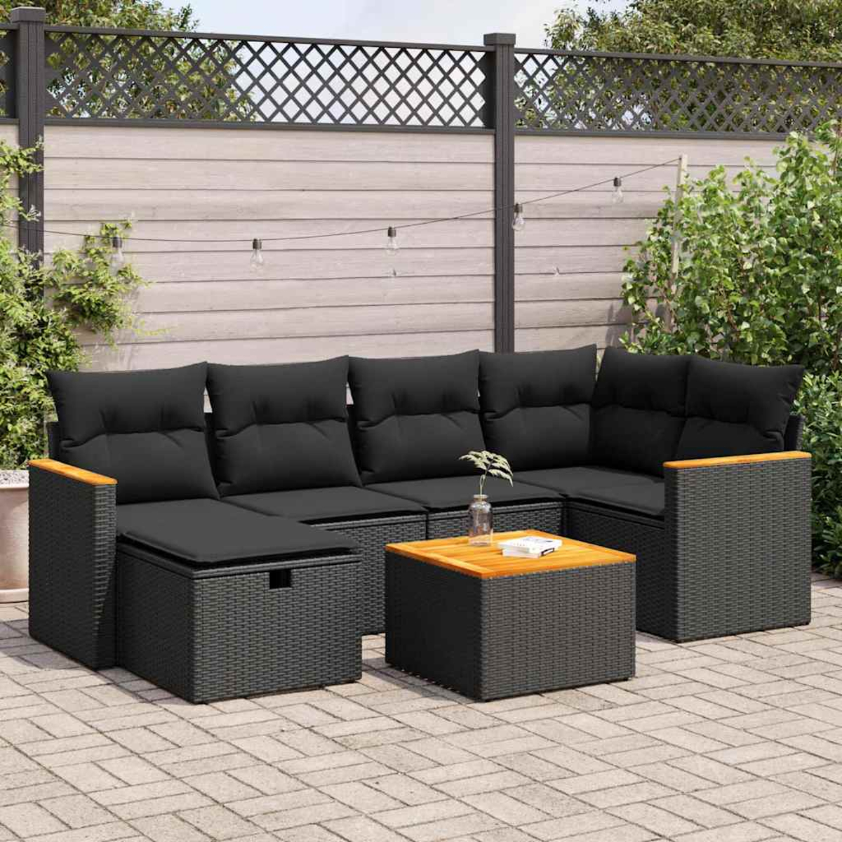 Set divani in vimini nero da esterno, con cuscini e tavolo in legno su patio in mattoni.