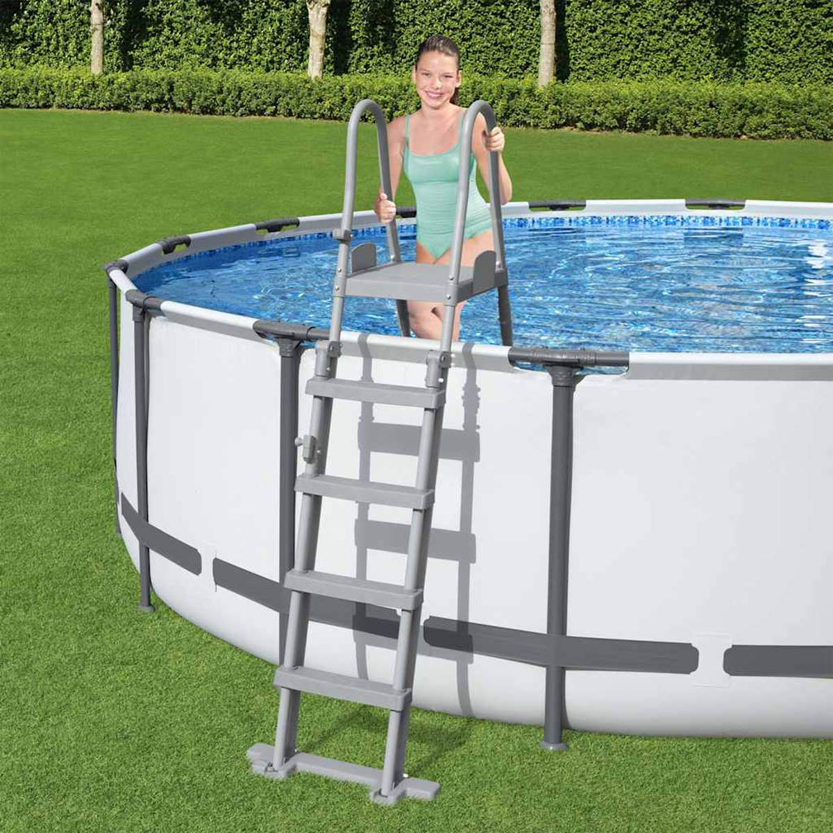 Frau in grünem Badeanzug im Pool, benutzt graue Leiter zum Aussteigen. Grünes Gras und Bäume im Hintergrund.