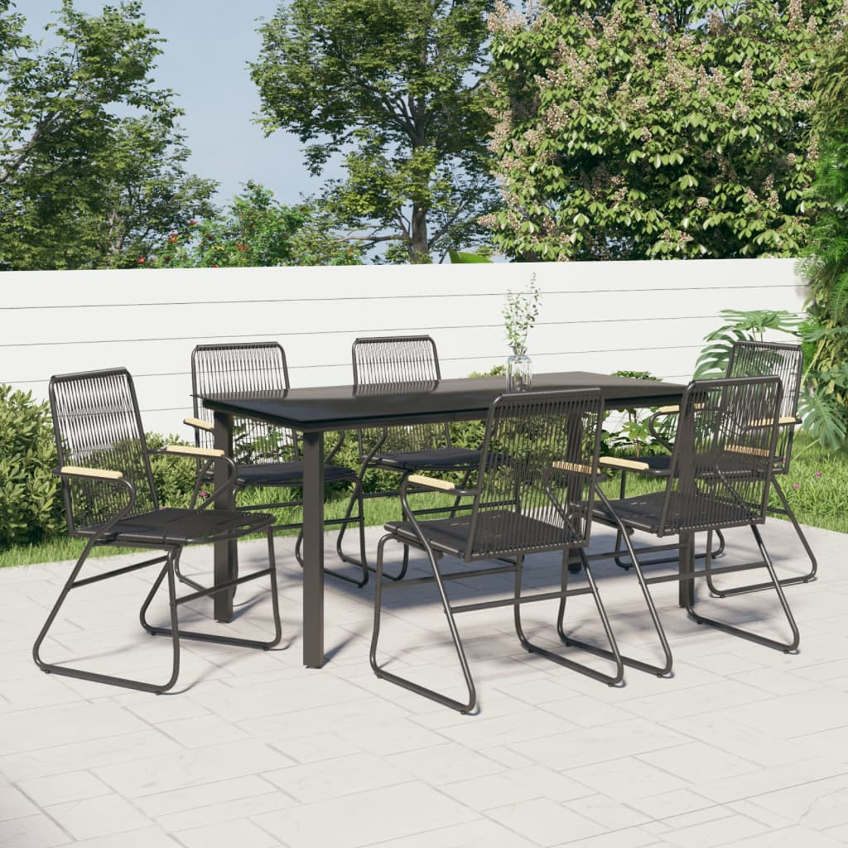 Eine Terrasse mit einem schwarzen Tisch und sechs schwarzen Stühlen. Im Hintergrund Bäume und ein weißer Zaun.