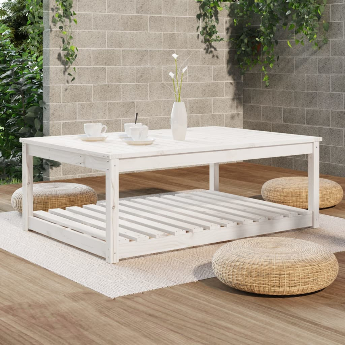 Ein weißer Holztisch mit unterem Regal und drei gewebten Hockern. Der Hintergrund ist eine Backsteinmauer.