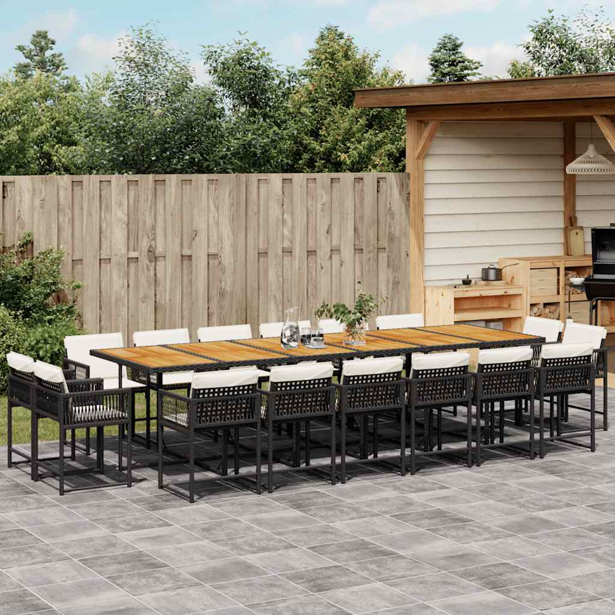 Essgruppe im Freien mit langem Tisch und Stühlen, auf einer Terrasse, mit Grün im Hintergrund.