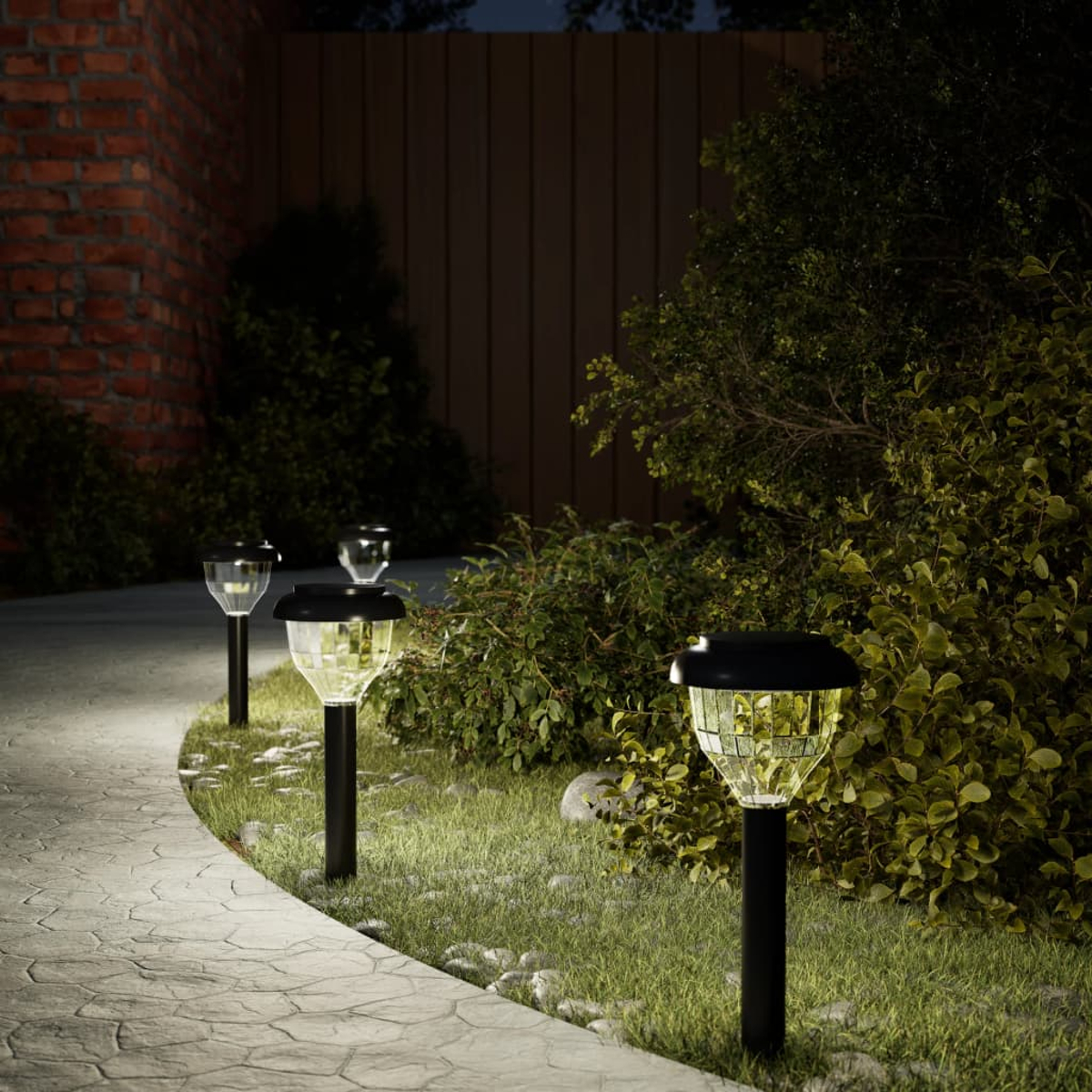 Tre luci solari da giardino illuminano un sentiero di pietra e la vegetazione circostante di notte.