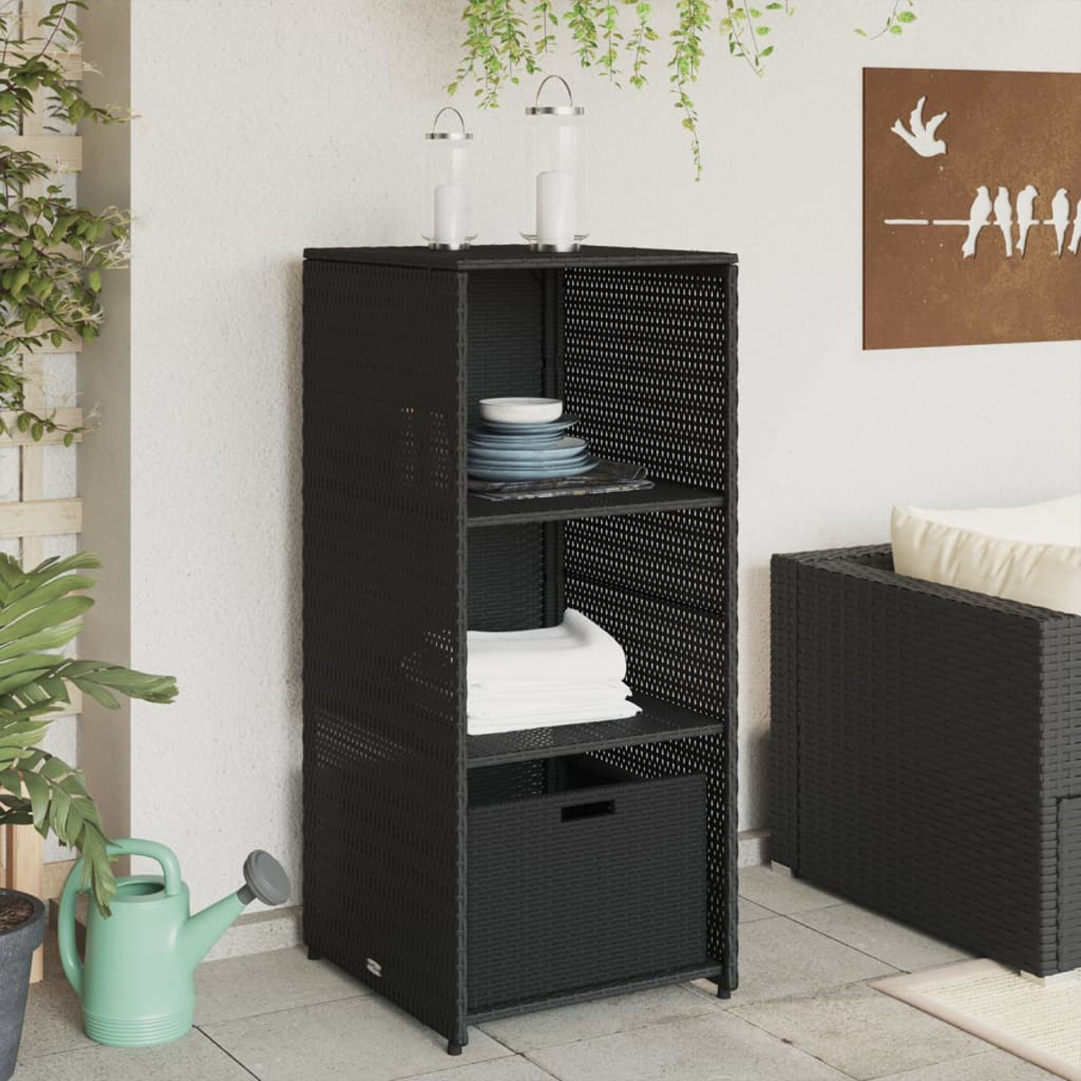 Schwarzes Korbgeflecht-Regal mit Gegenständen. Eine Gießkanne und ein kleines Sofa sind in der Nähe.