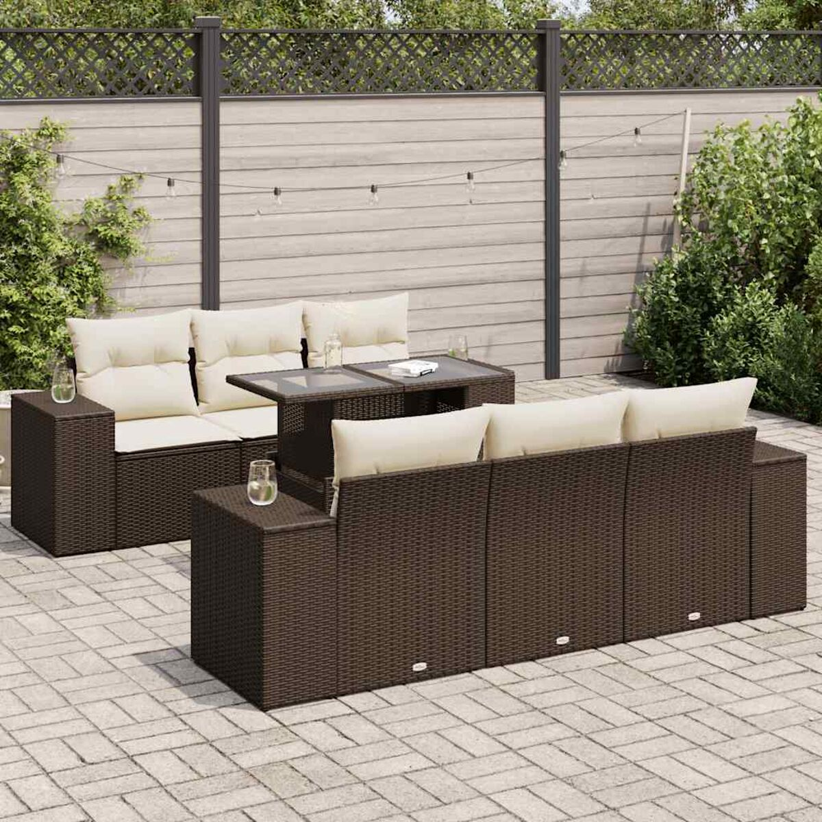 Juego de sofás de ratán marrón con mesa con tapa de cristal y cojines beige. En un patio.