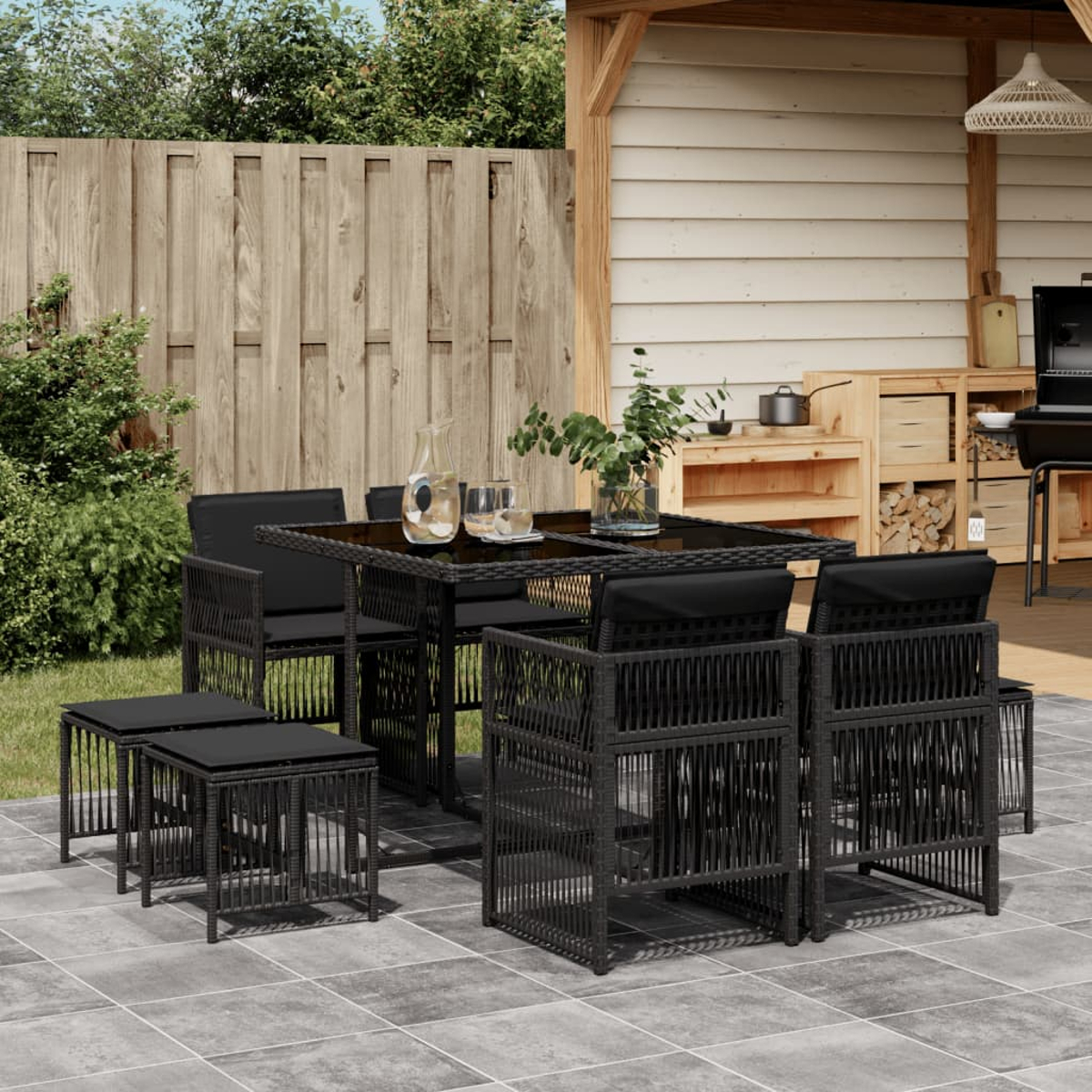 Schwarzes Ess-Set für den Außenbereich aus Korbgeflecht auf einer Terrasse. Enthält Tisch, Stühle und kleine Hocker.