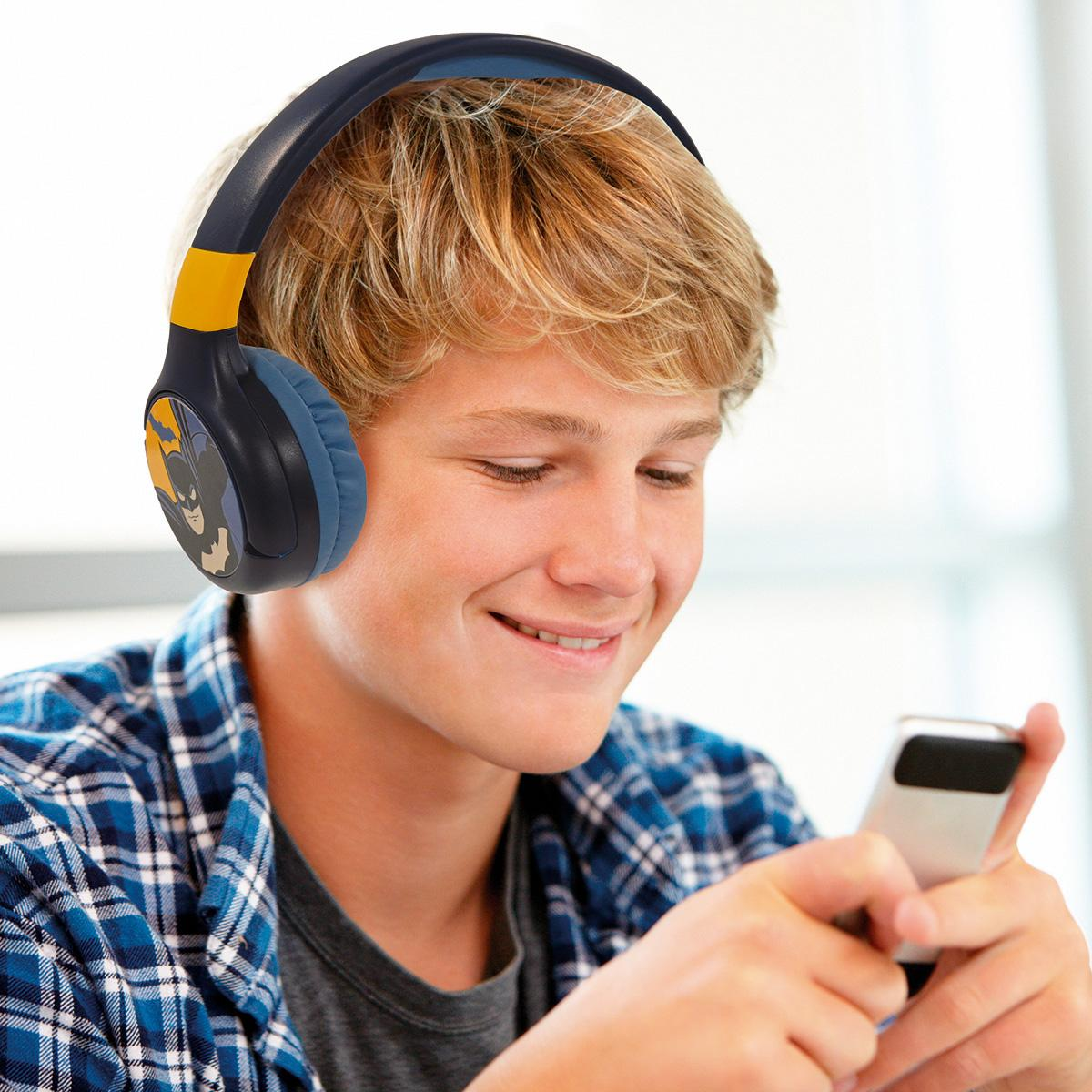 Ragazzo adolescente con cuffie Batman, sorridente a uno smartphone. Ha i capelli biondi e indossa una camicia a quadri.