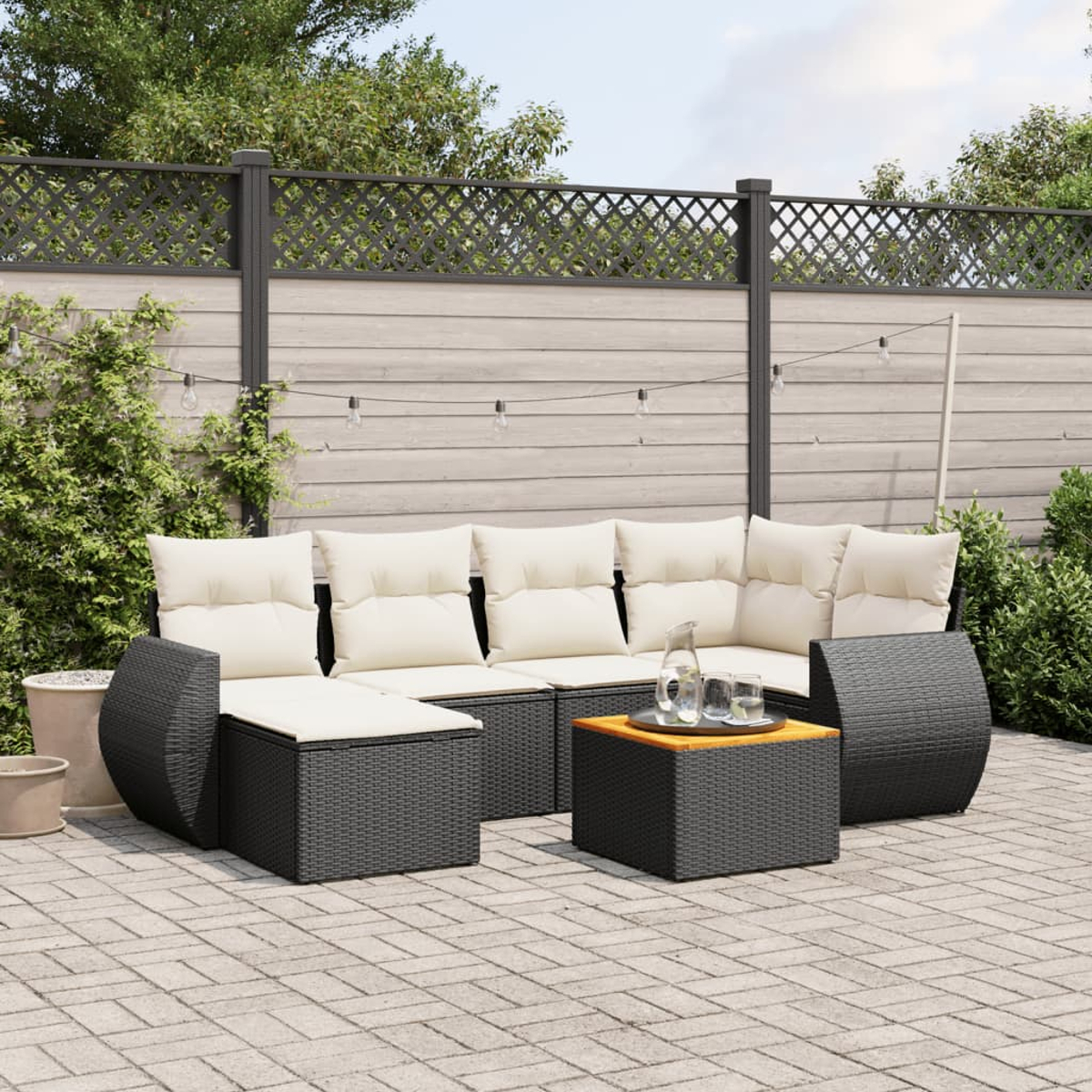 Ein schwarzes Outdoor-Ecksofa aus Korbgeflecht mit weißen Kissen, einem Tisch und einem Holzzaun.