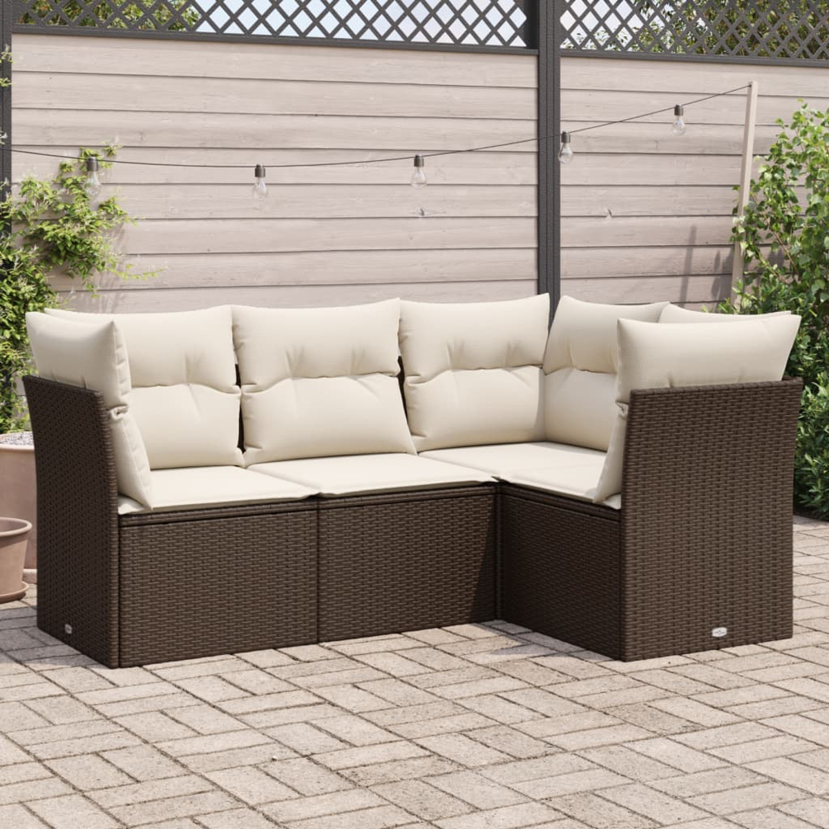 Braunes Rattansofa mit cremefarbenen Kissen auf einer Backsteinterrasse, in der Nähe eines Holzzauns.