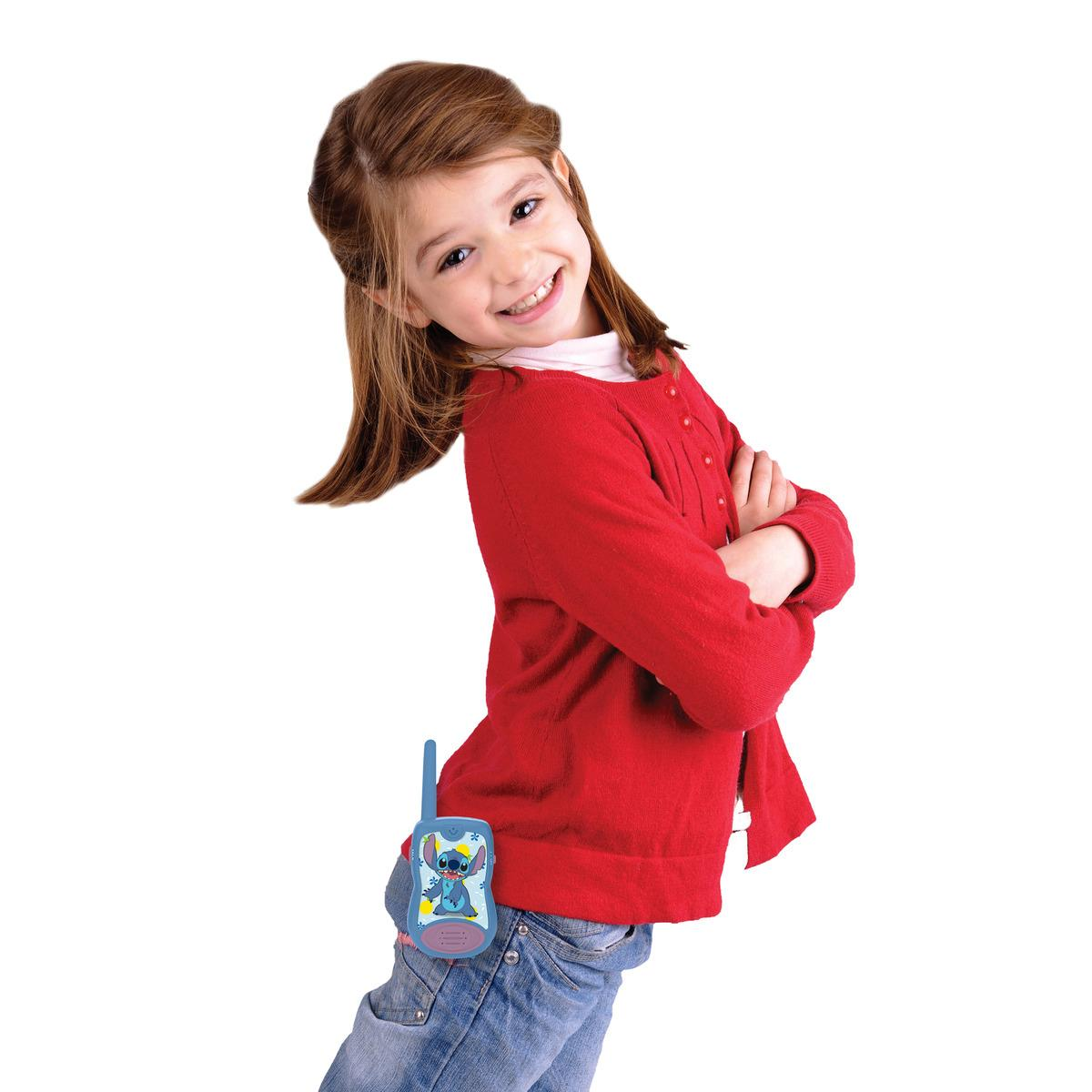 Młoda dziewczyna w czerwonym swetrze i niebieskich dżinsach trzyma zabawkowe walkie-talkie.