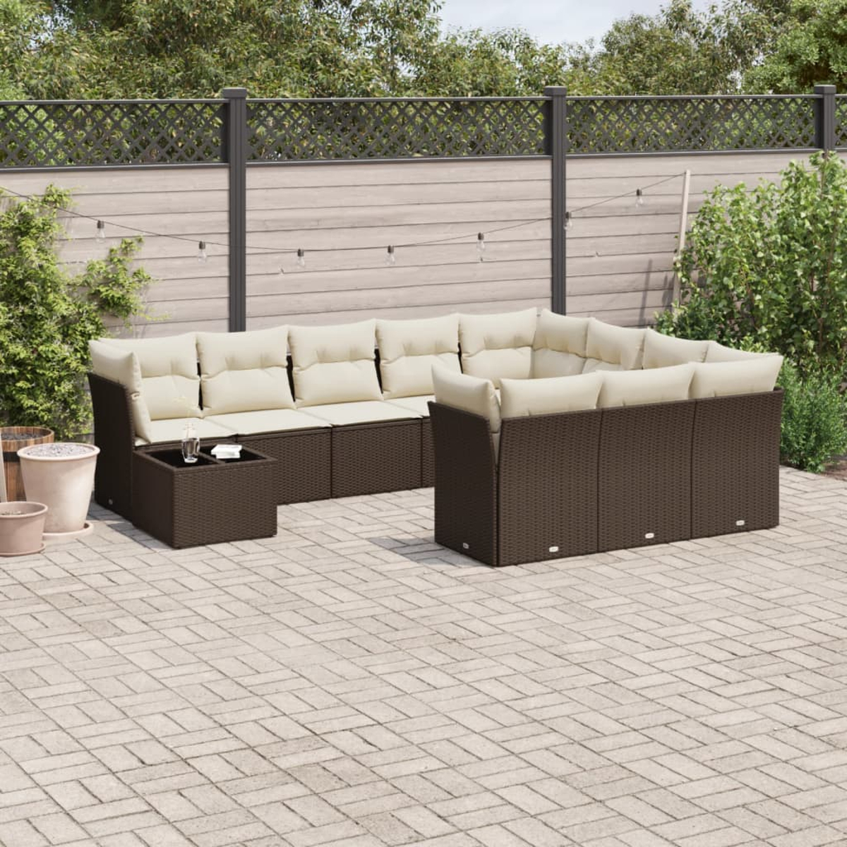 Divano angolare marrone da esterno con cuscini e tavolo color crema. Patio con verde e recinzione.