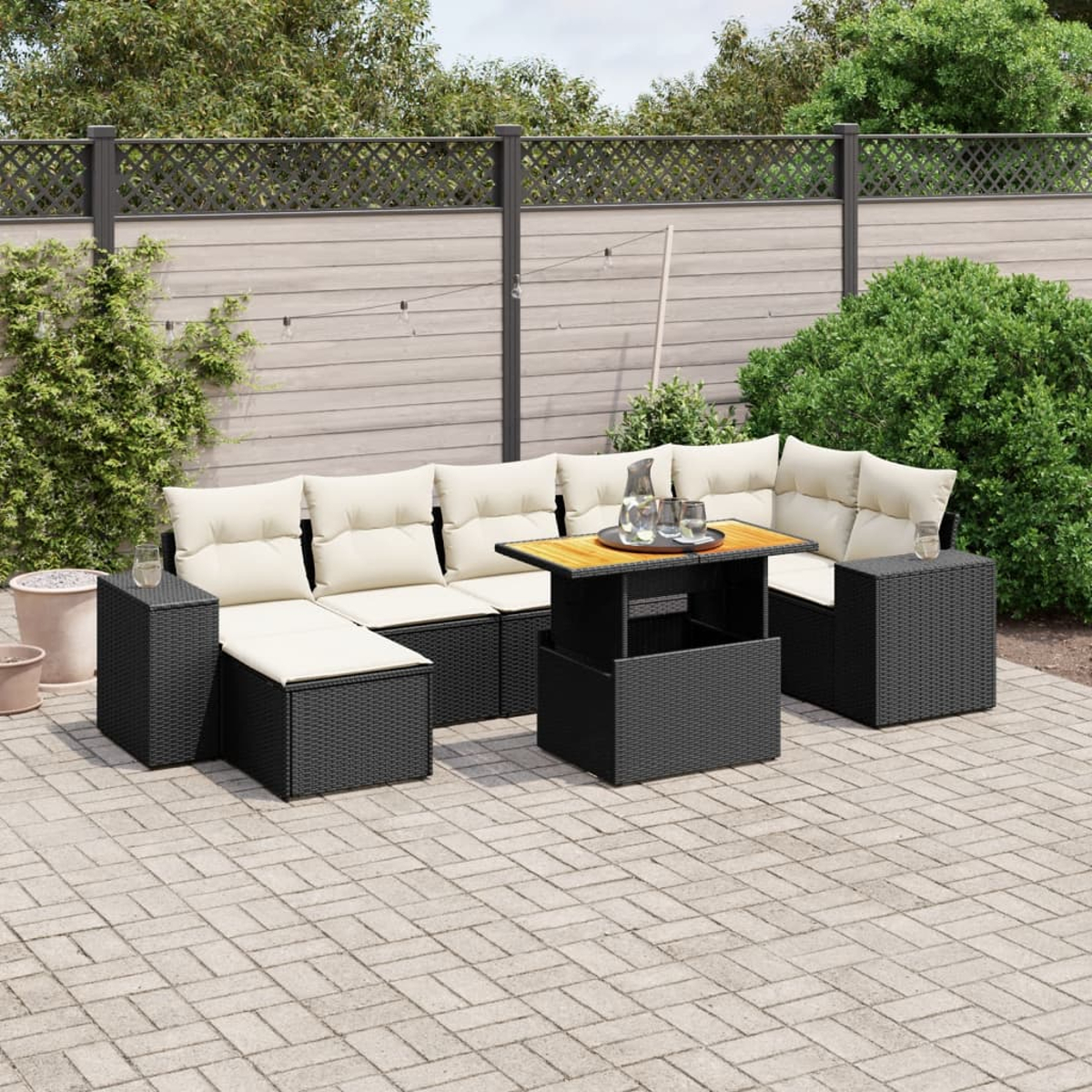 Schwarzes Outdoor-Sofaset aus Korbgeflecht. Beige Kissen. Tisch höhenverstellbar. Backstein-Patio, Zaun, Pflanzen.