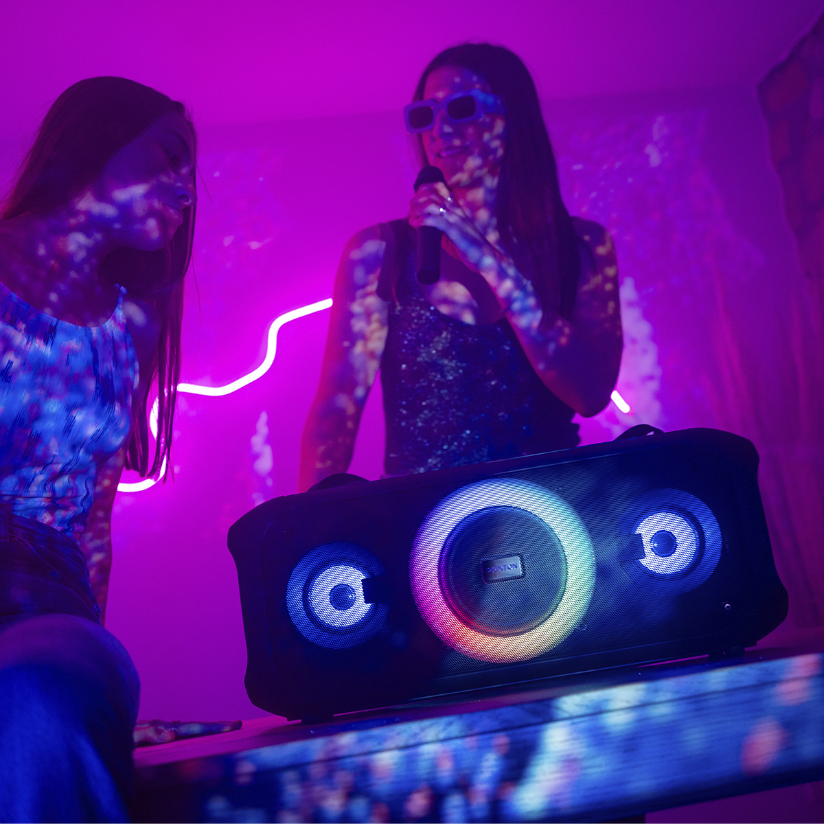 Dwie kobiety, jedna śpiewa i głośnik. To ustawienia karaoke z neonami.