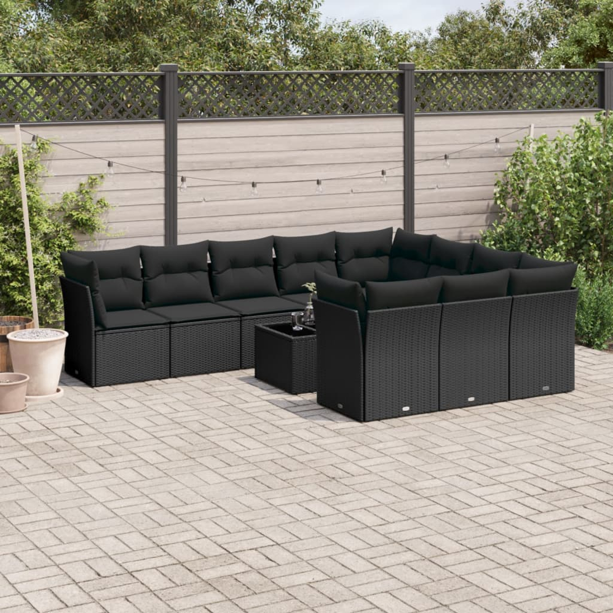 Ein schwarzes Ecksofa aus Korbgeflecht für den Außenbereich mit schwarzen Kissen. Ein Tisch und eine Terrasse sind sichtbar.