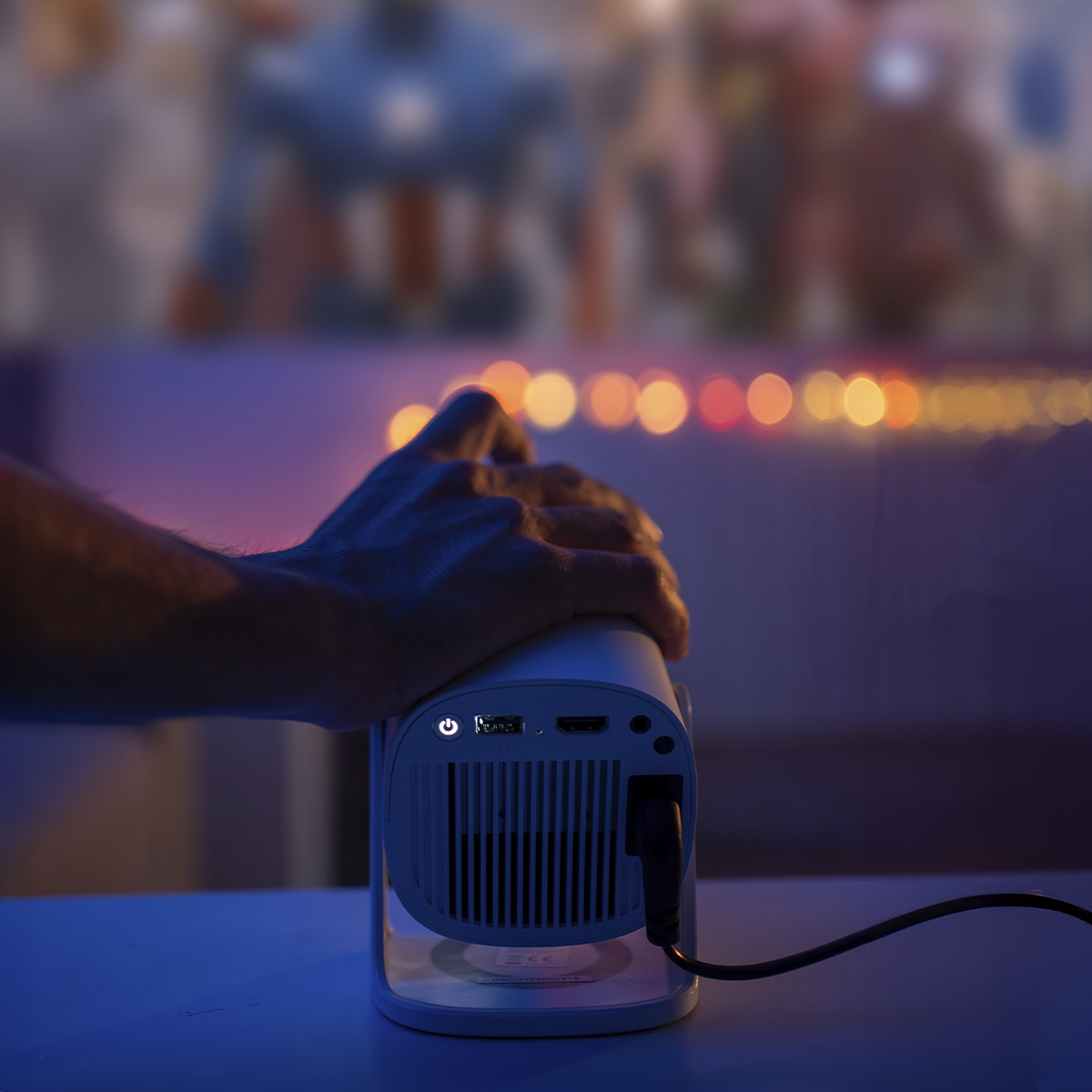 Ręka osoby reguluje biały projektor z świecącym światłem, z rozmytą sceną filmową w tle.