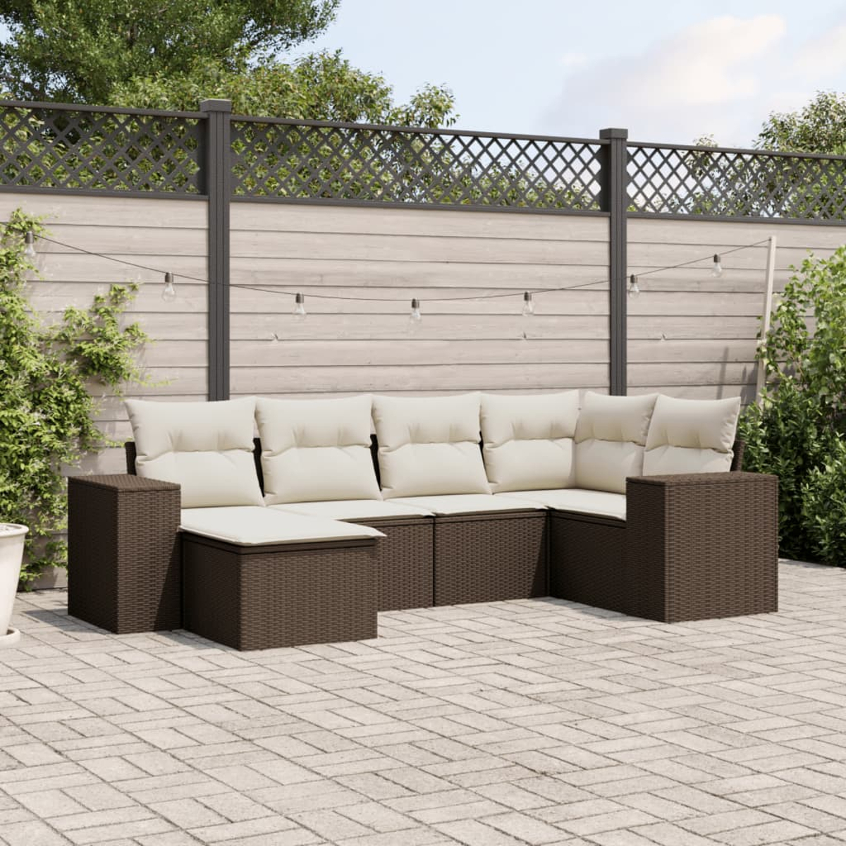 Set di mobili da patio esterno. Divano in vimini marrone, tavolo e cuscini. Patio pavimentato e recinzione in legno.